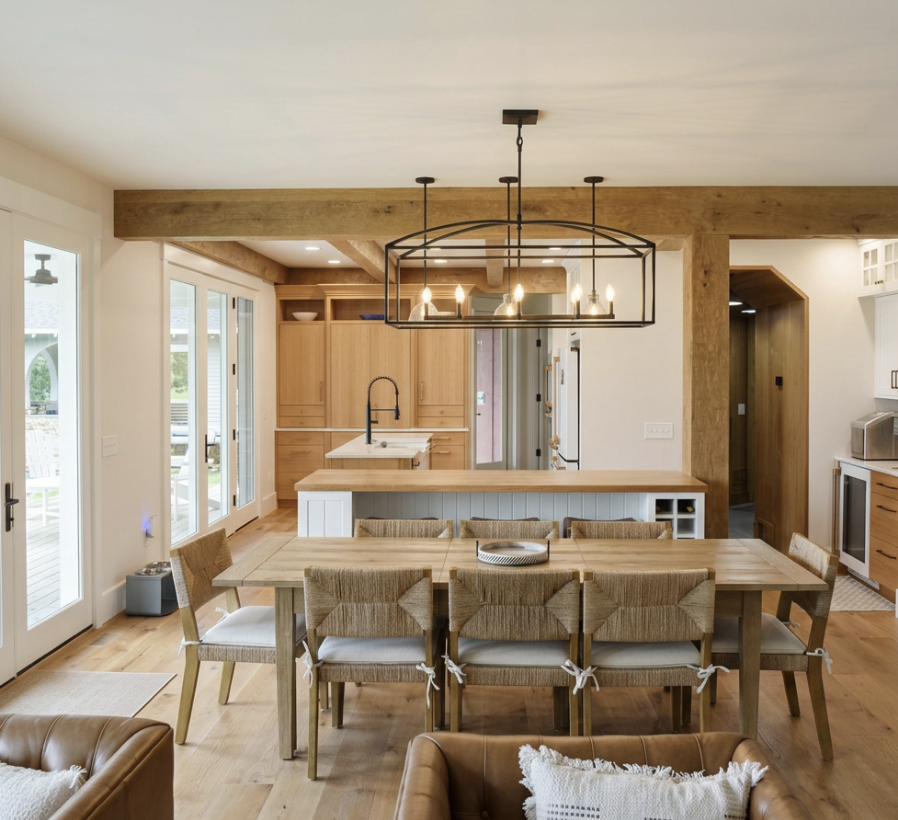 Open-plan kitchen and dining area with wood finishes, large dining table with eight chairs, a chandelier above, a kitchen island with a black faucet, and sliding glass doors leading outside.