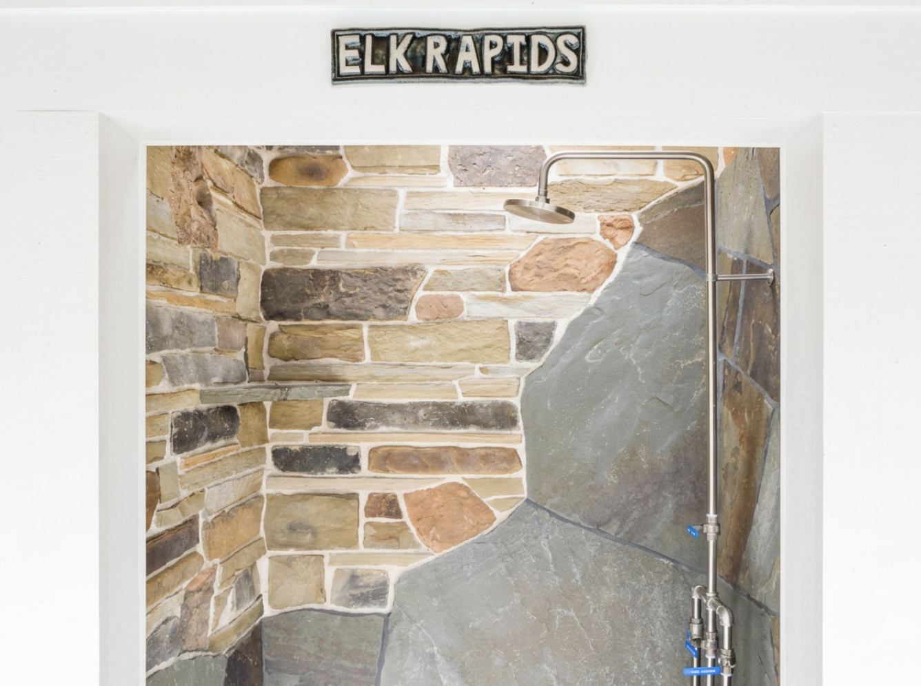 A shower area with a stone wall and a metal showerhead, labeled 'ELK RAPIDS' sign above the opening.
