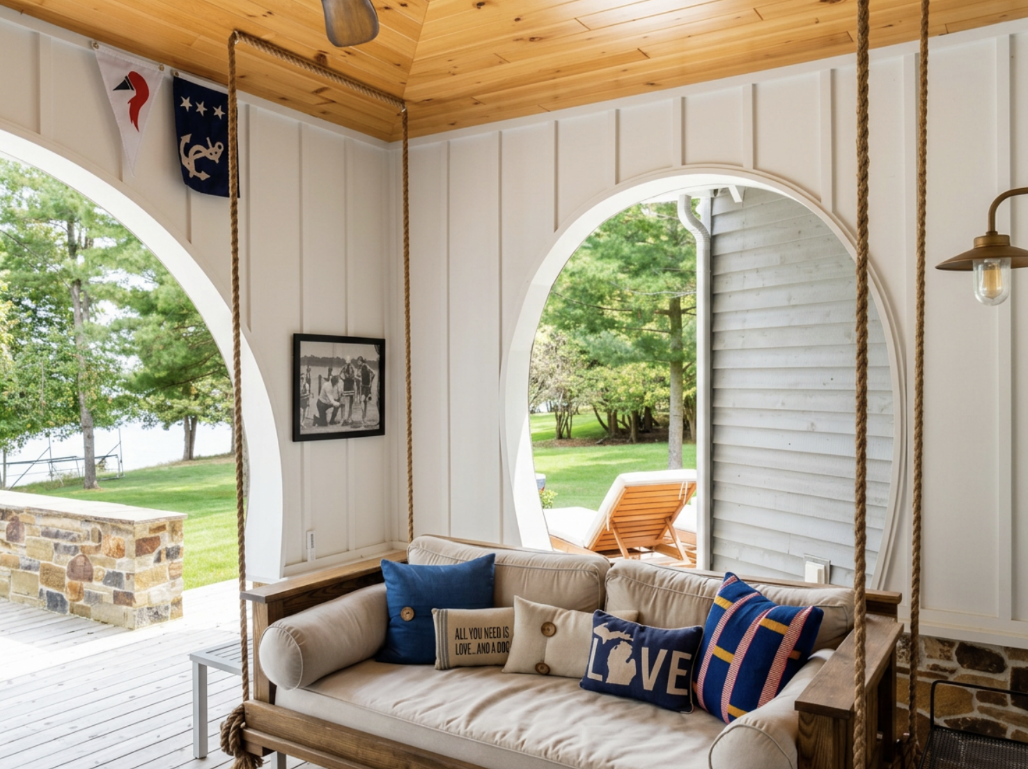 Porch swing with pillows on a screened porch, overlooking a green yard and lake.