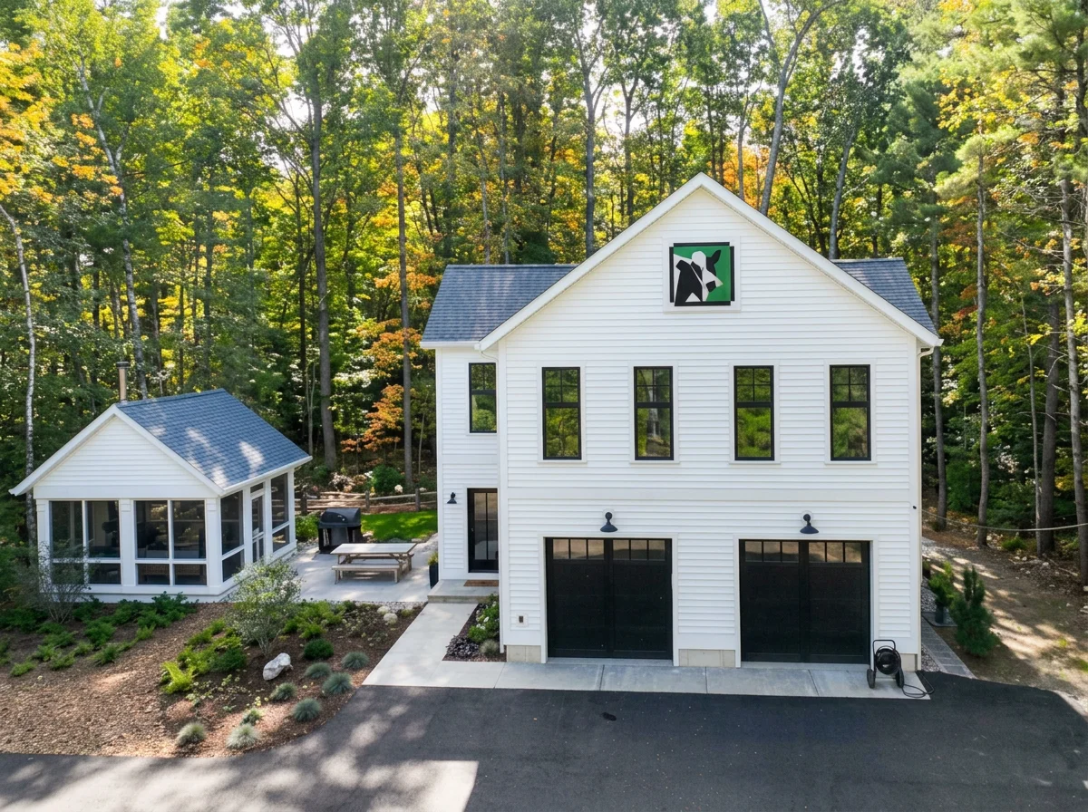 Modern white house with black garage doors, surrounded by trees, with a screened porch and outdoor seating area.