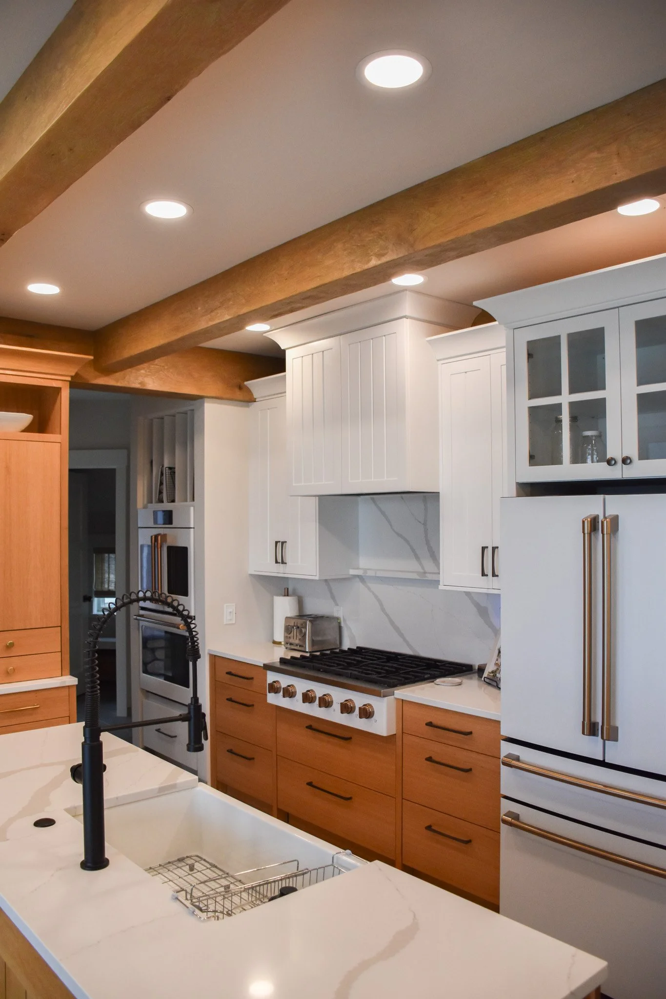 Modern kitchen with white upper cabinets, wooden lower cabinets, a white marble backsplash, a gas stove, and a white marble countertop island with a black faucet.