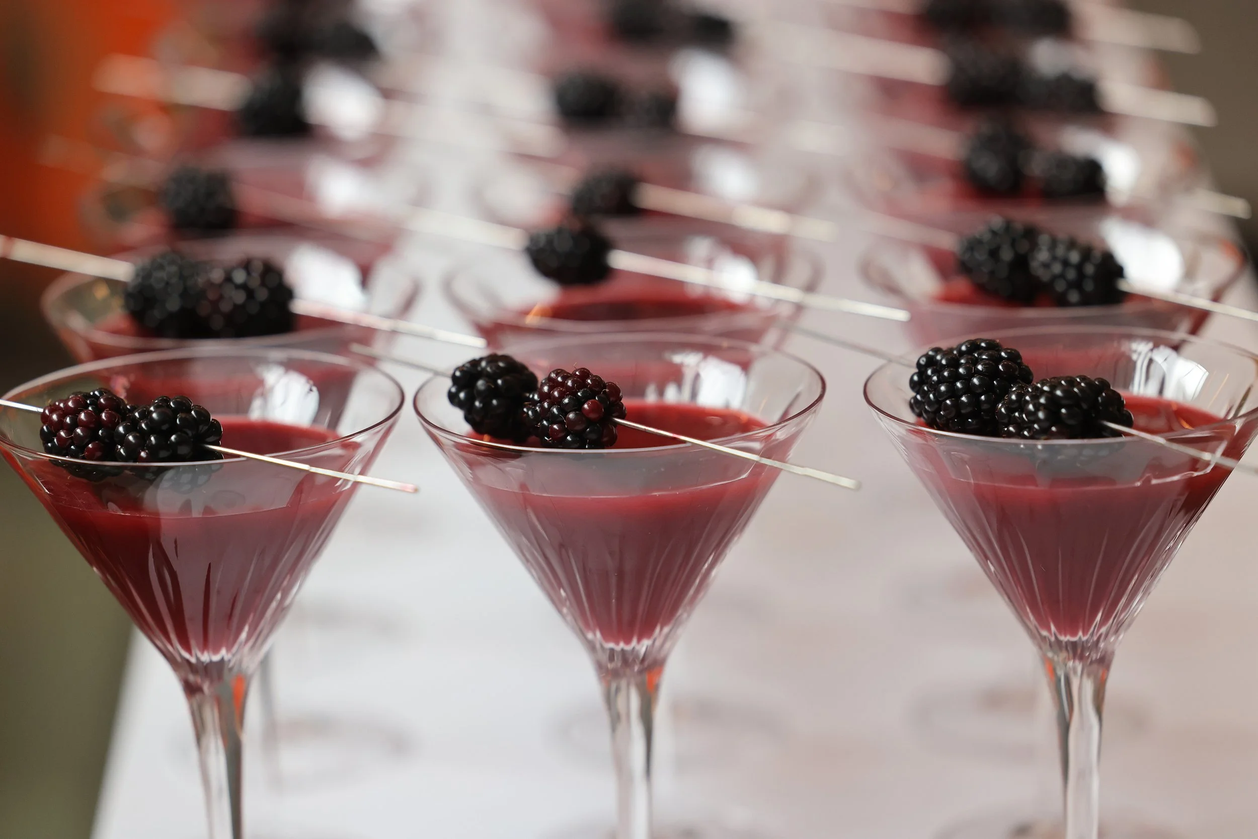 Copas de cóctel con líquido rojo y moras negras decorativas en la parte superior.