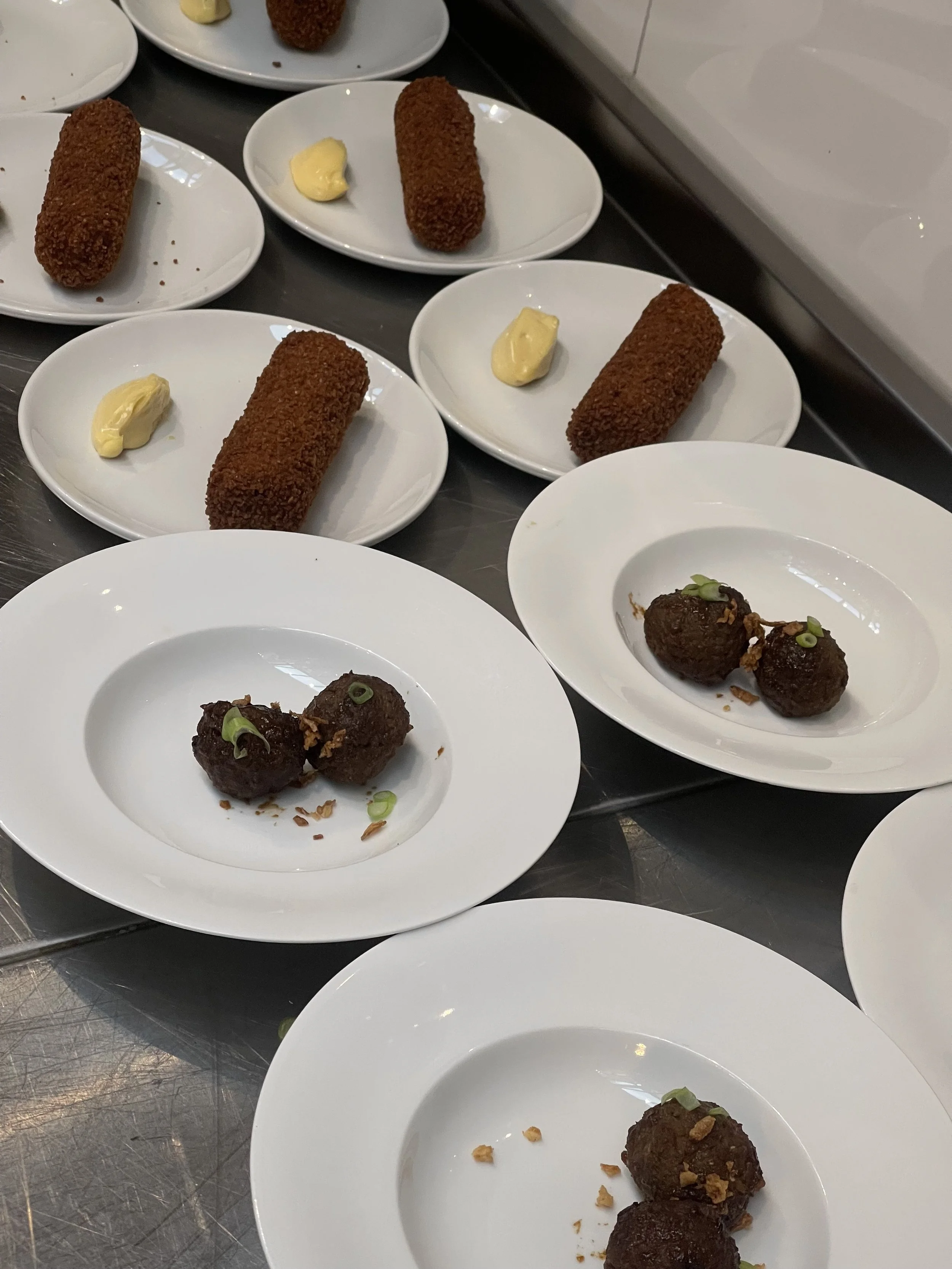 Platos con croquetas empanizadas y bolas de carne o albóndigas en salsas distintas, acompañados de pequeñas porciones de guarniciones o salsas.