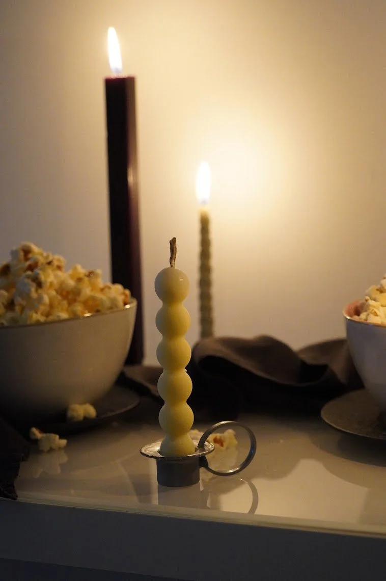 Vela de mantequilla en un soporte metálico sobre una mesa, con flamas encendidas en el fondo, flanqueada por tazones de palomitas de maíz