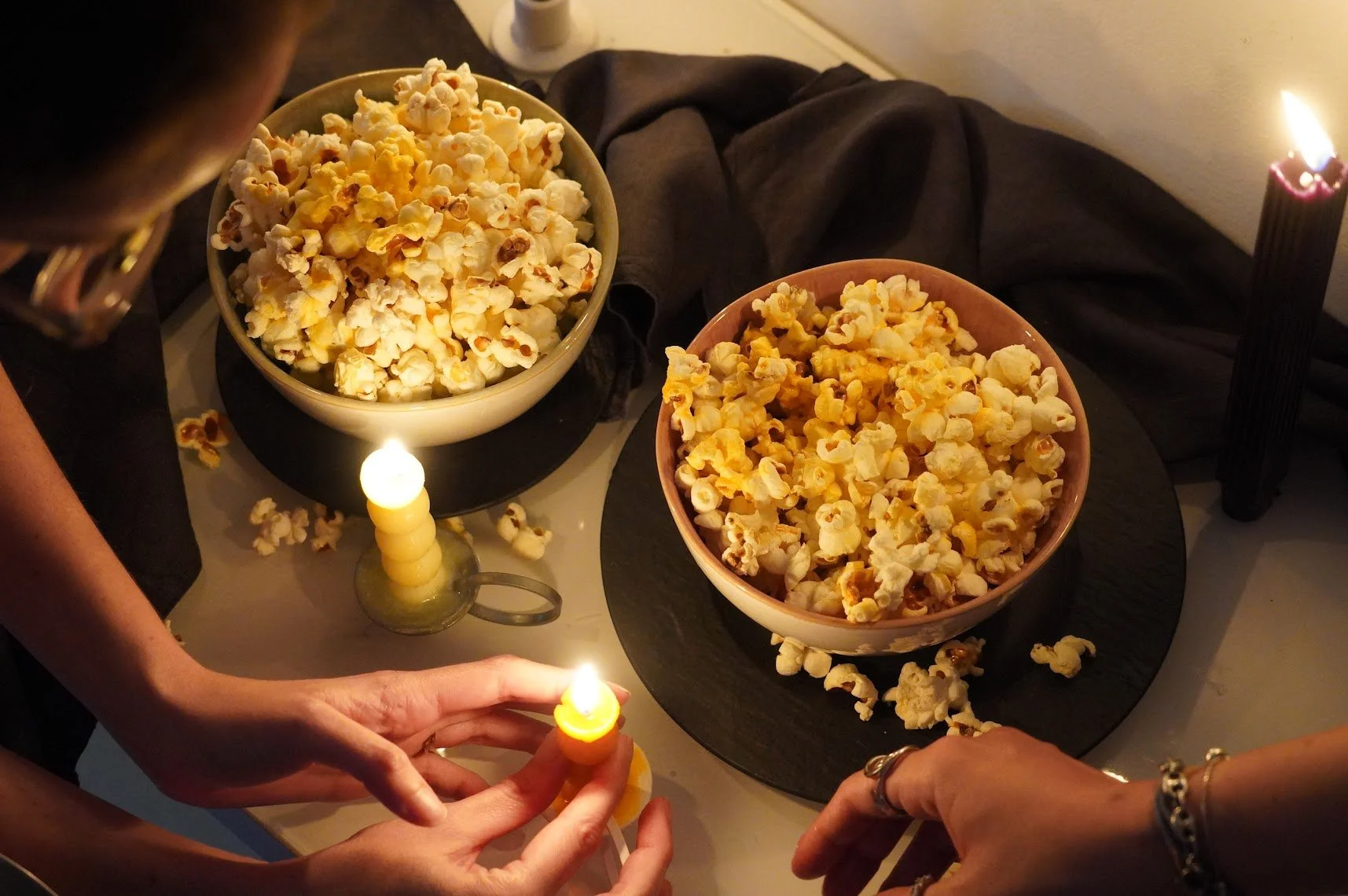 Personas quemando velas de mantequilla y distribuyéndola en palomitas de maíz en una mesa con dos cuencos grandes, uno con palomitas blancas y otro con palomitas de color amarillo.