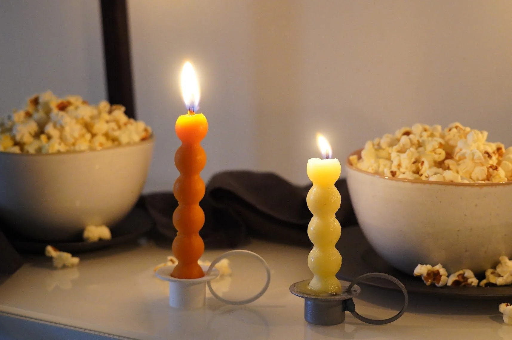 Velas de mantequilla encendidas junto a tazones de palomitas de maíz en una mesa.