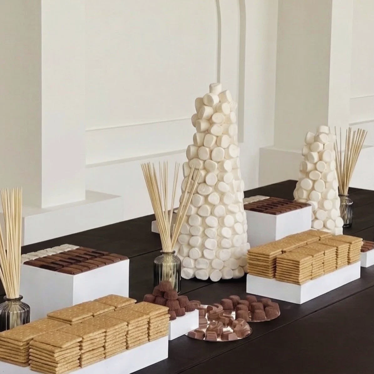 Display de dulces y galletas en tonos neutros con varillas de madera en jarrones transparentes, sobre fondo blanco minimalista.