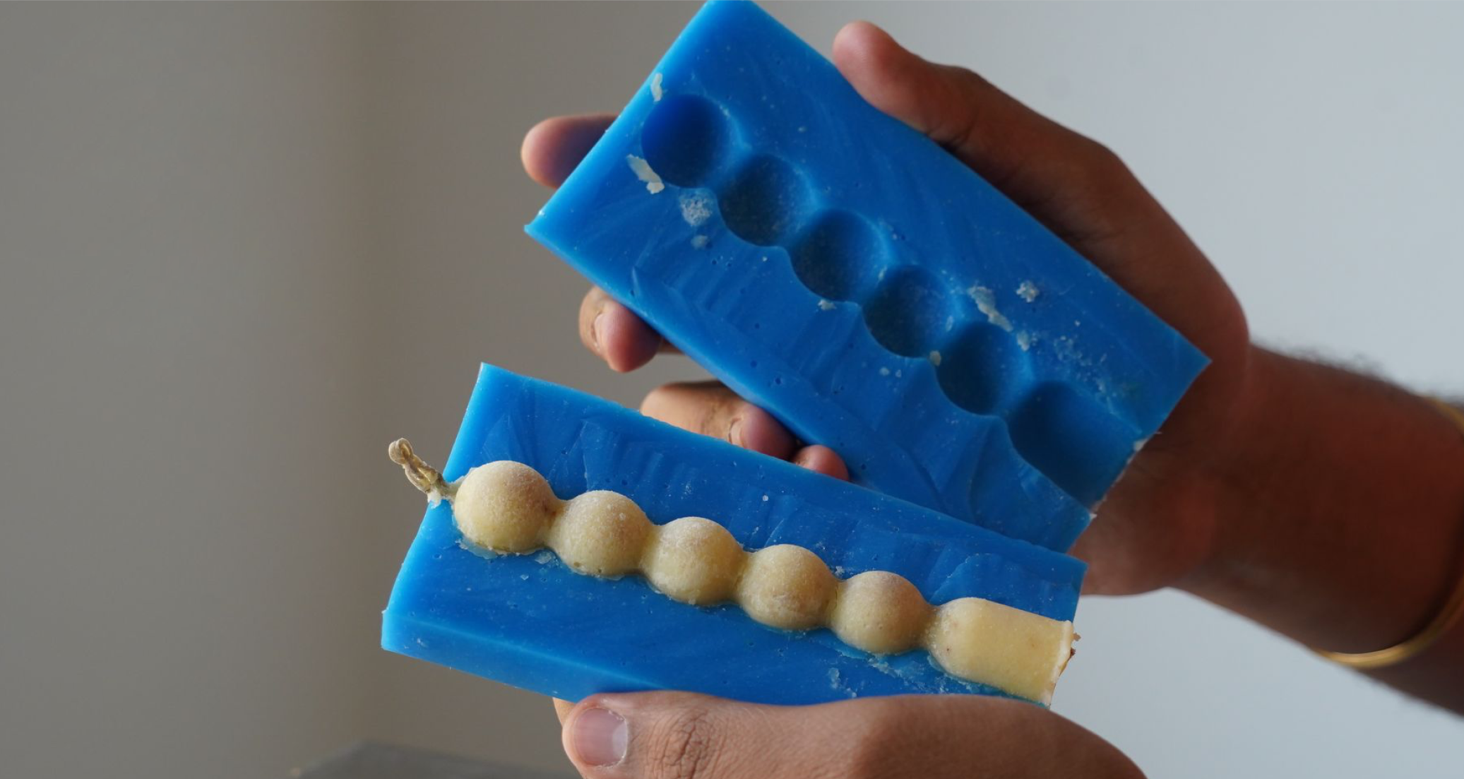 Mano sosteniendo molde de silicon, una de ellas contiene una vela de mantequilla.