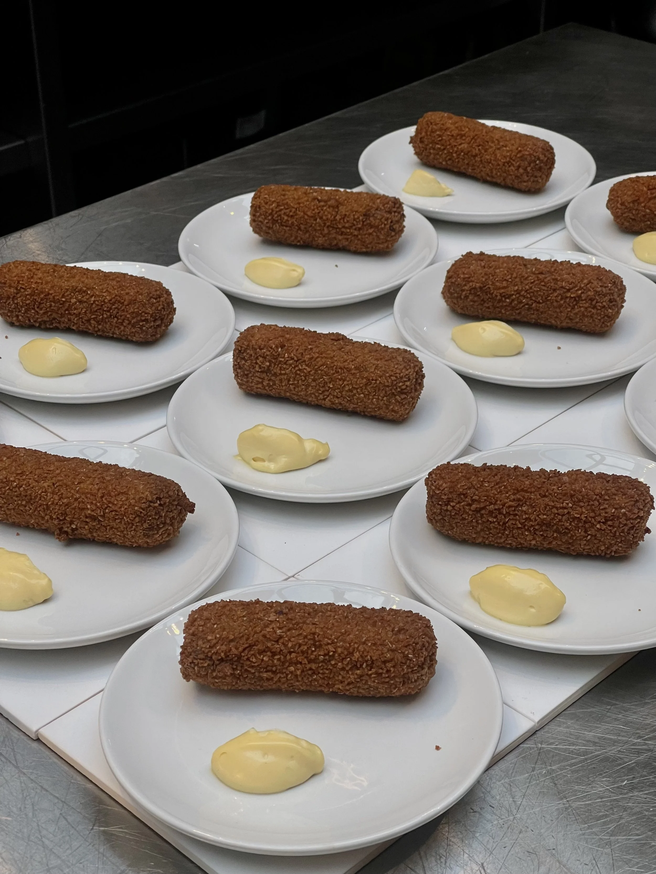 Platos con croquetas empanizadas acompañadas de mayonesa en platos blancos sobre mesa de cocina.
