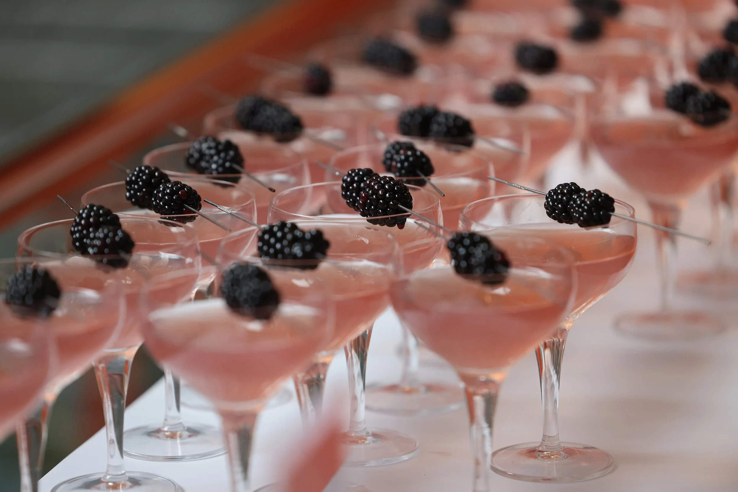 Copas de postre con mousse rosa y frambuesas negras decorativas encima.