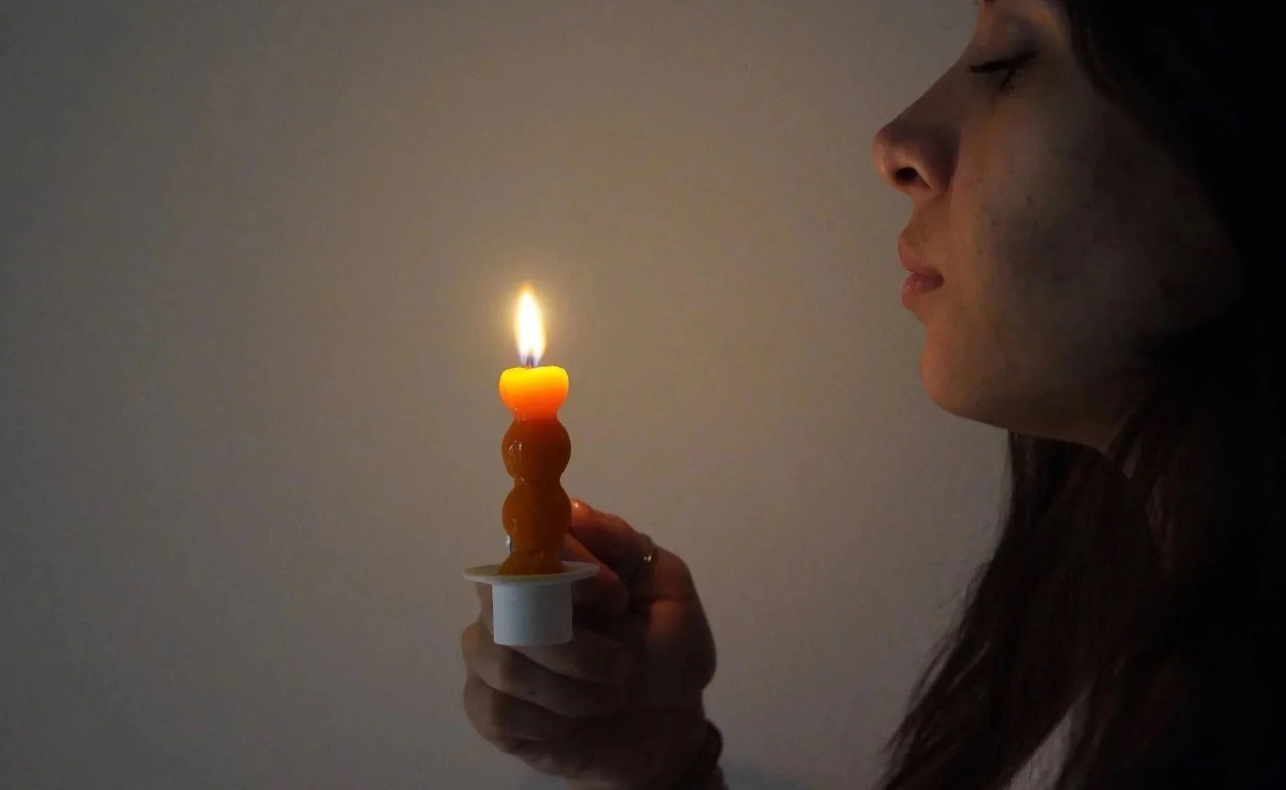 Mujer sosteniendo una vela de mantequilla en forma de espiral con una llama encendida, en un fondo oscuro.
