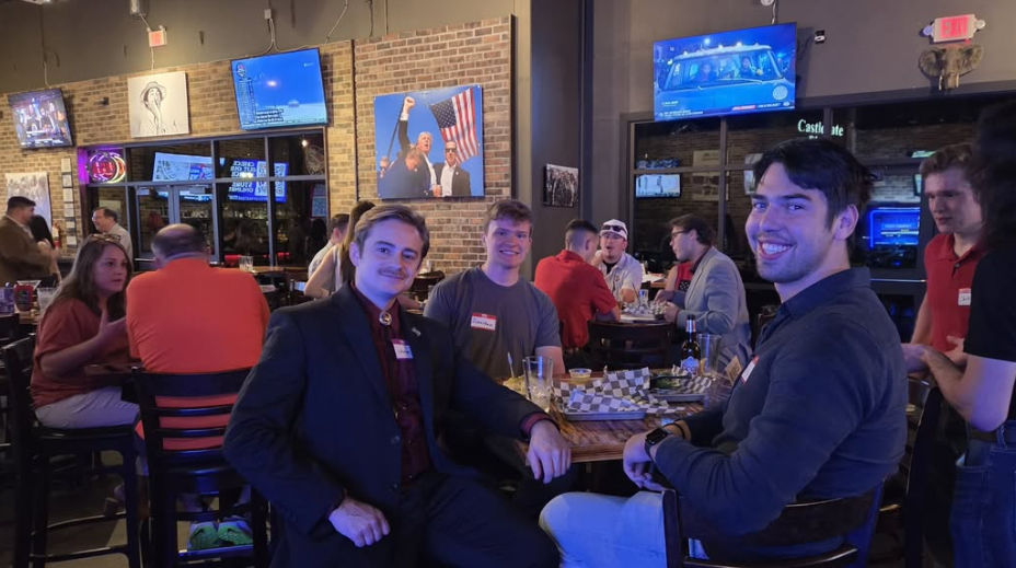 Group of people socializing at a sports bar with televisions, drinks, and American-themed wall art