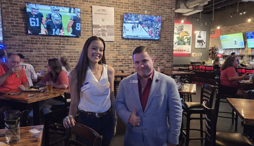Two people posing inside a sports bar with televisions showing football and hockey games.