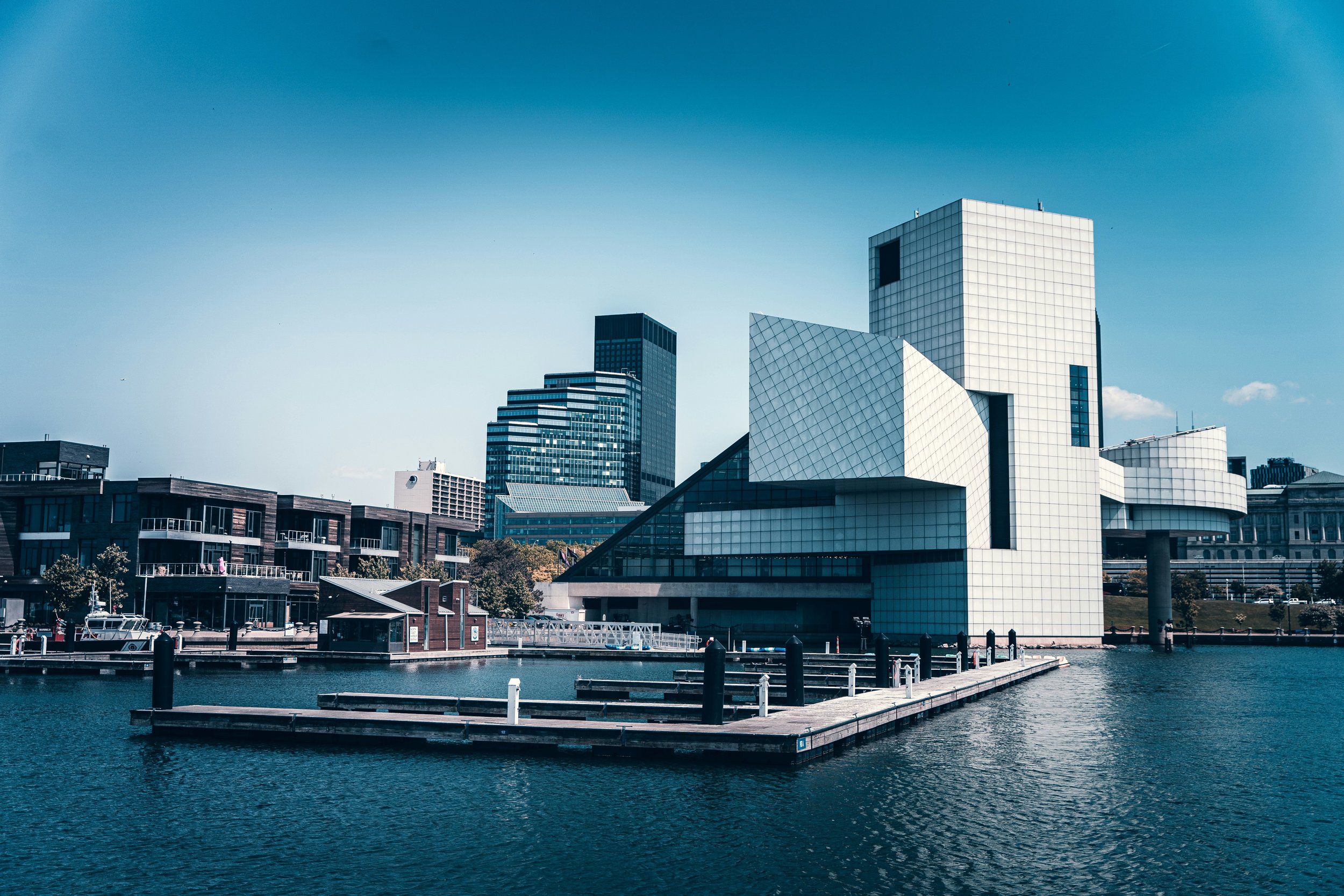 Modern waterfront cityscape with high-rise buildings, a marina with boats, and a clear blue sky.