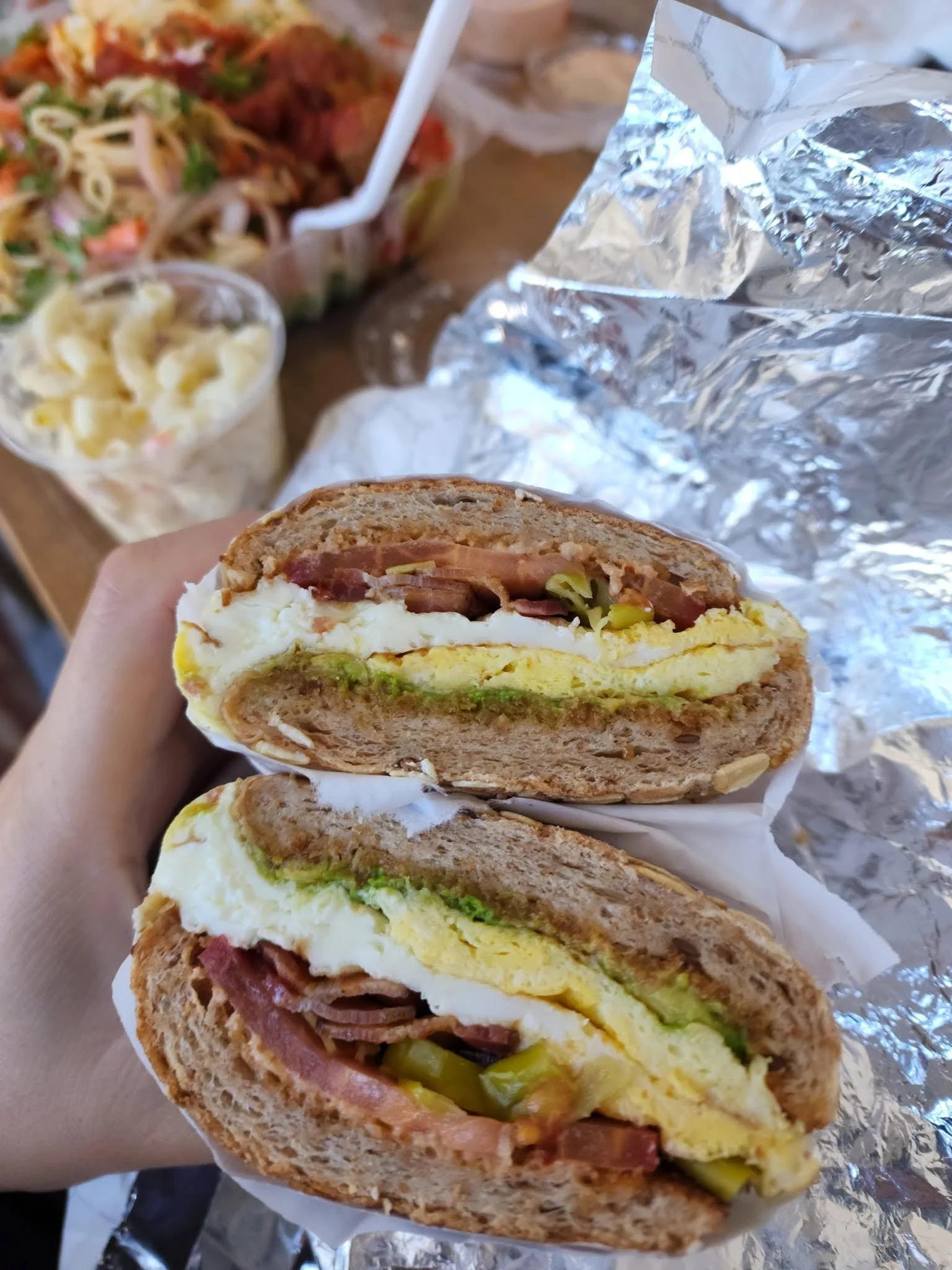 Half of a sandwich with layers of ham, eggs, lettuce, and pickles, wrapped in foil.