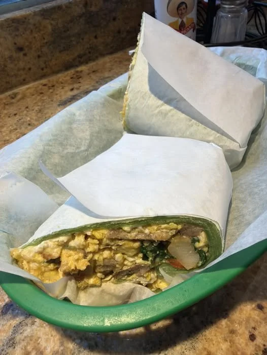 Cutting-egg burrito wrapped in white paper inside a green basket on a marble counter.