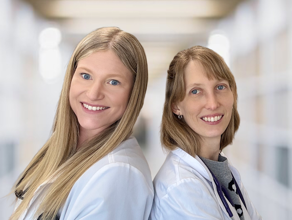 Two female healthcare professionals in a hospital corridor smiling at the camera