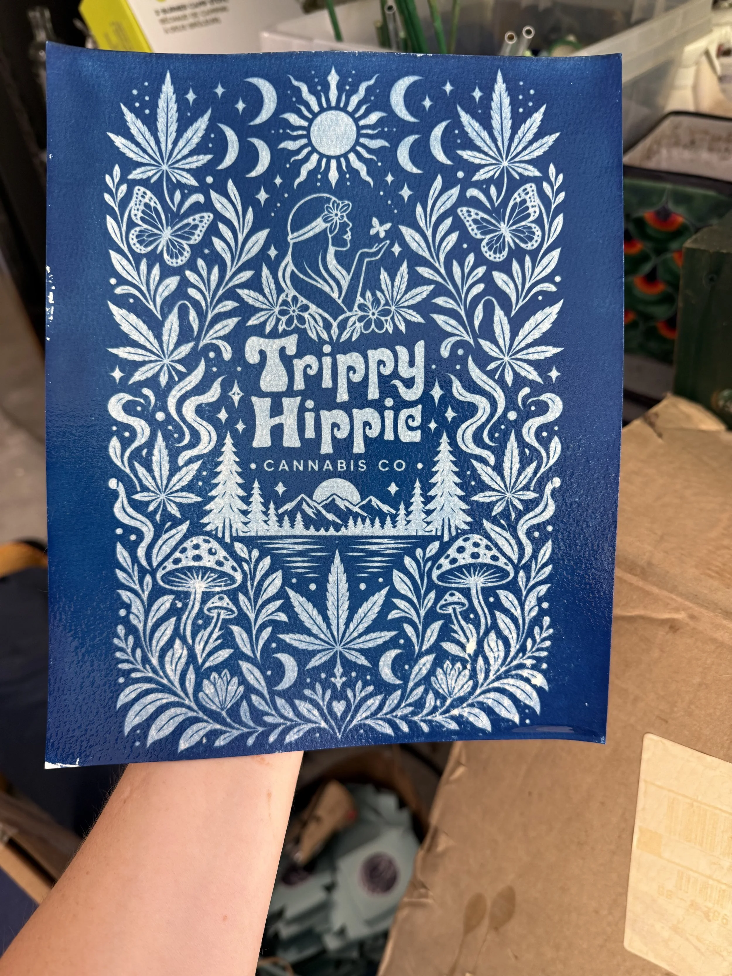 Blue paper with white psychedelic art featuring a woman, cannabis leaves, butterflies, mushrooms, mountains, the sun, and moons, with the text "Trippy Hippie Cannabis Co."