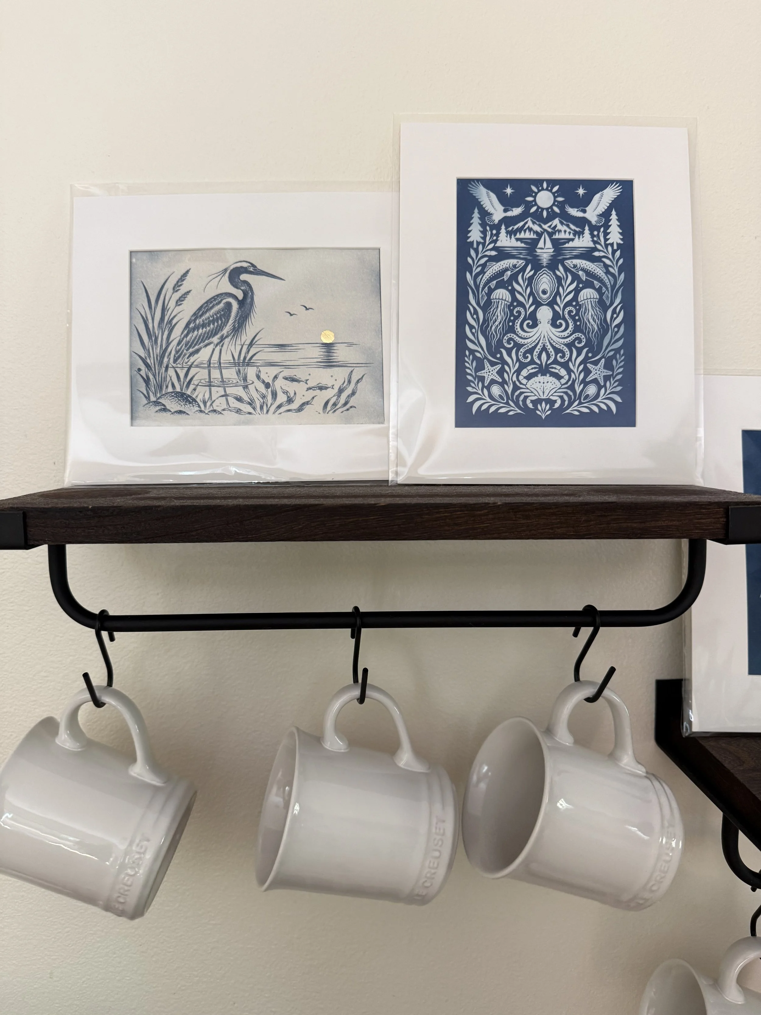 Six white coffee mugs hanging on hooks beneath a black shelf, with black hooks on a white wall.