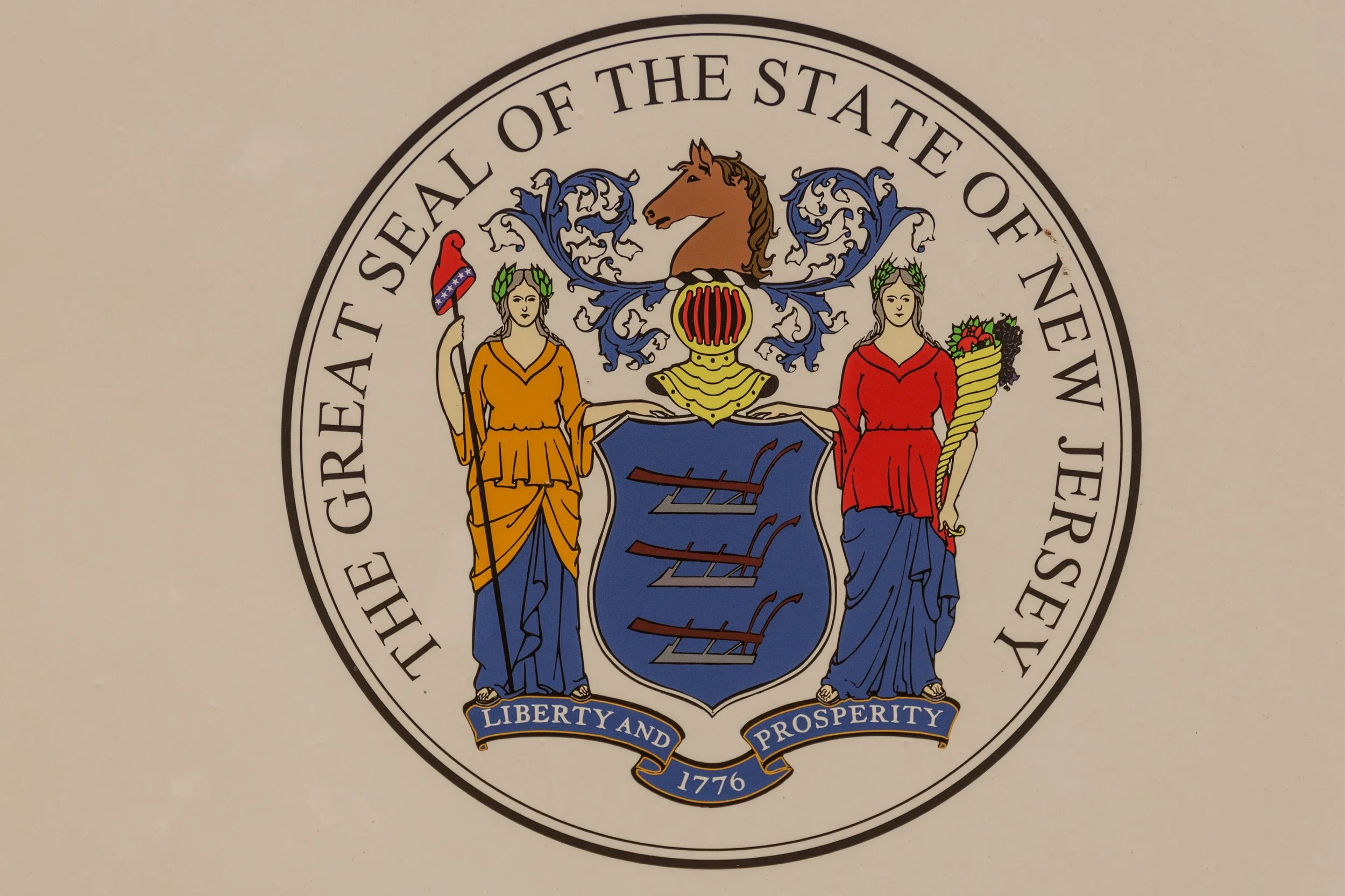 The Great Seal of the State of New York, featuring two female figures holding a shield with a ship, a crest with a horse head, and a banner with the motto 'Liberty and Prosperity' along with the year 1776.