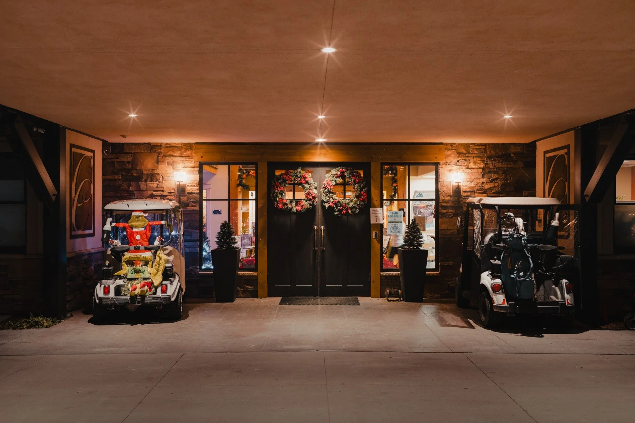 The clubhouse entrance at night, with wreaths on the doors and golf carts parked on either side.