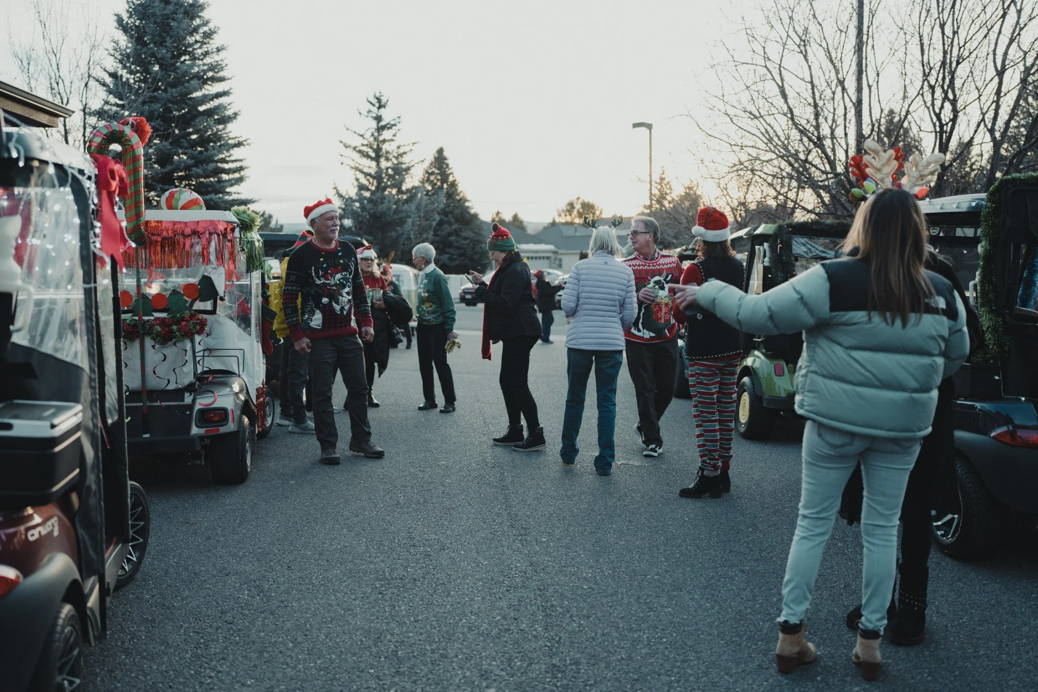 Members in holiday sweaters and festive headwear gather between rows of decorated golf carts.