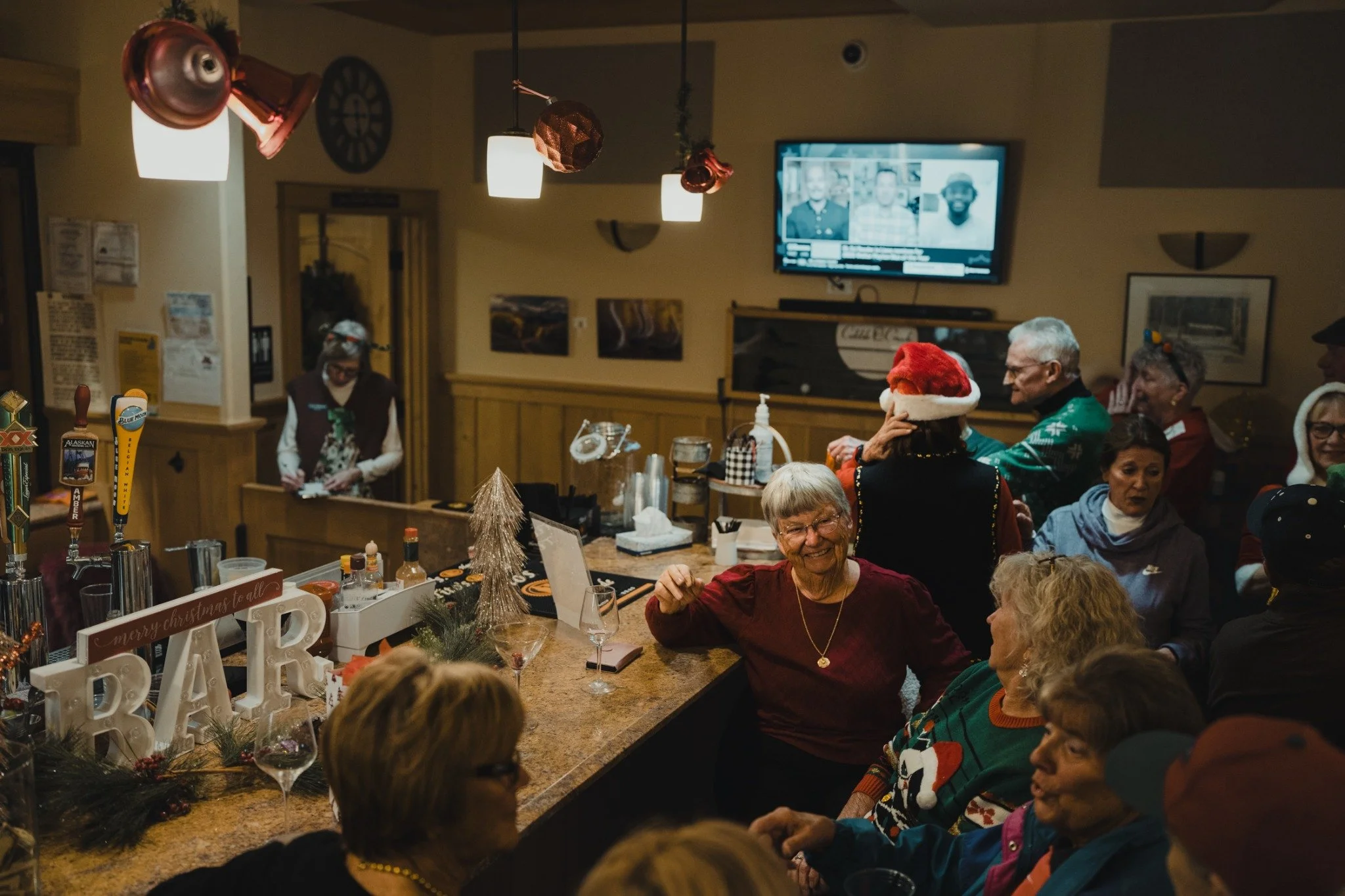 A gathering around the Tavern bar, with holiday decorations, festive sweaters, and people in conversation.