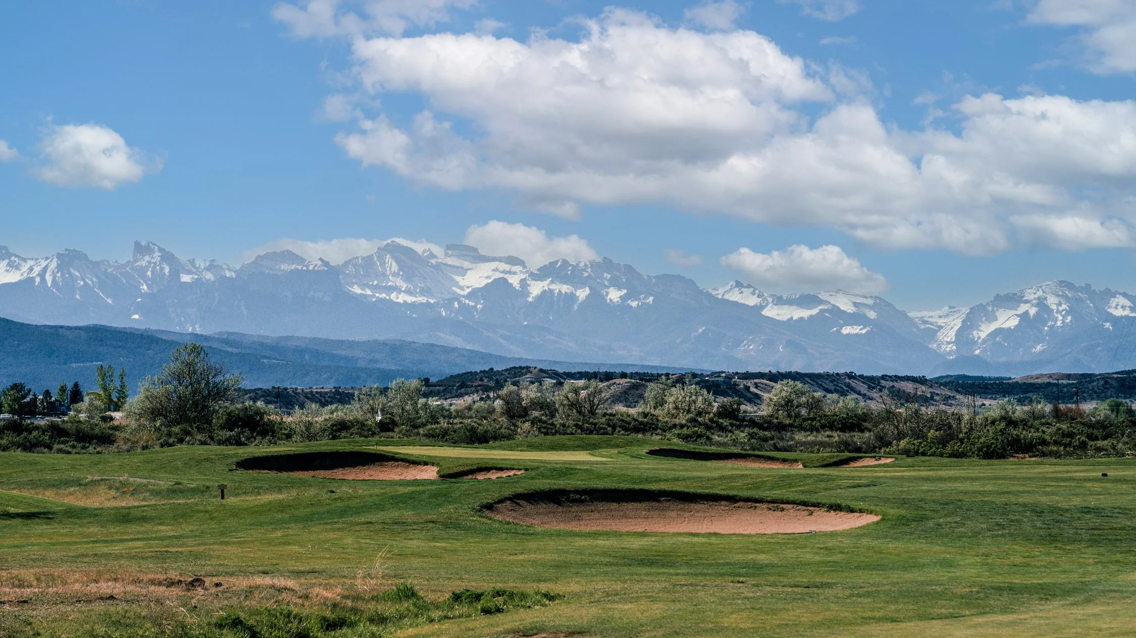 The thirteenth green at Cobble Creek in spring, guarded by bunkers beneath the snow-covered Cimarron Mountains.