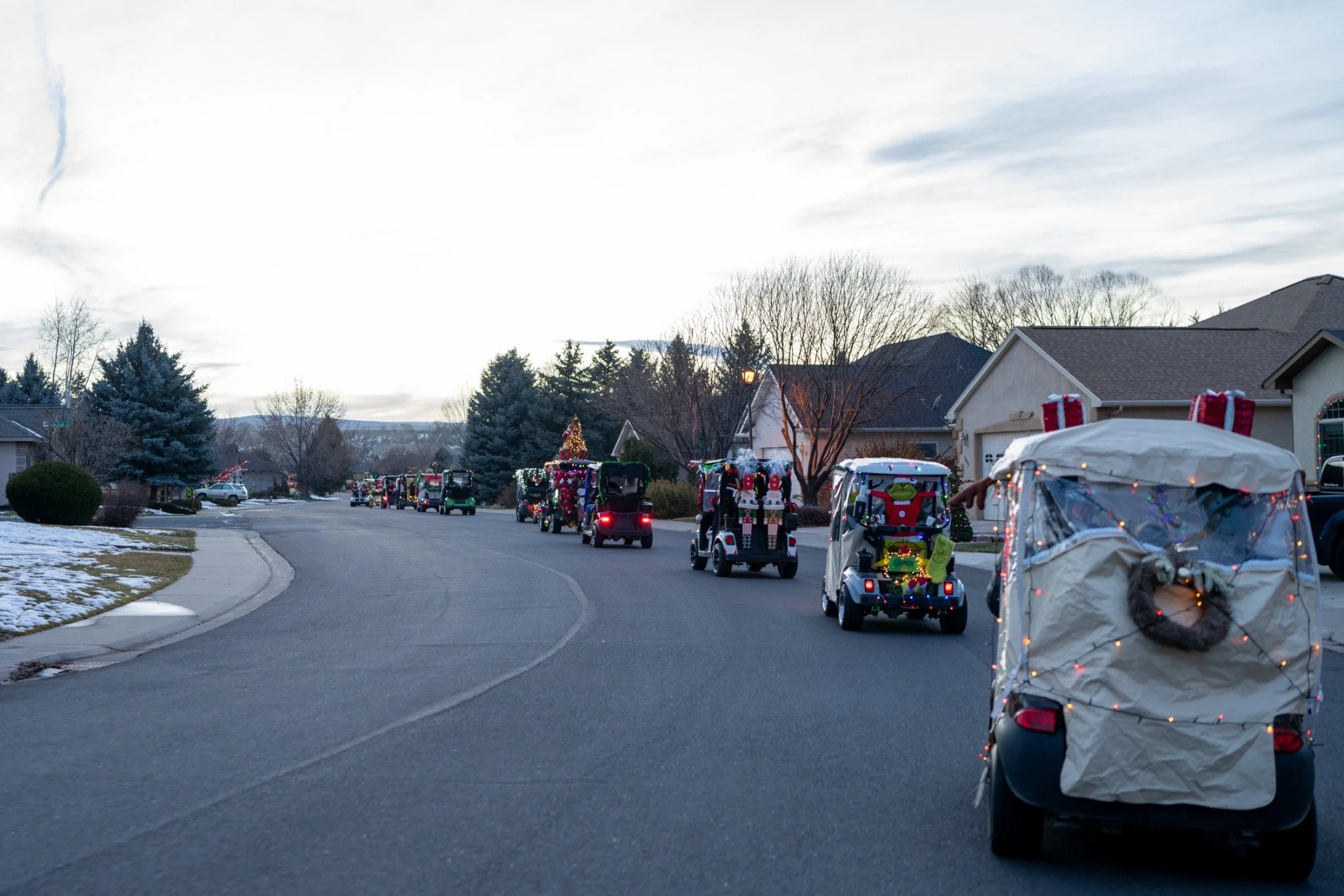 A procession of decorated golf carts travels through the Cobble Creek neighborhood, past lawns with patches of snow.