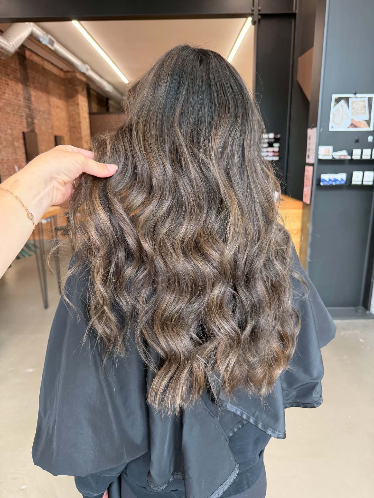 Back view of shoulder-length brunette hair with soft waves and dimensional highlights by Caitlyn Deming.