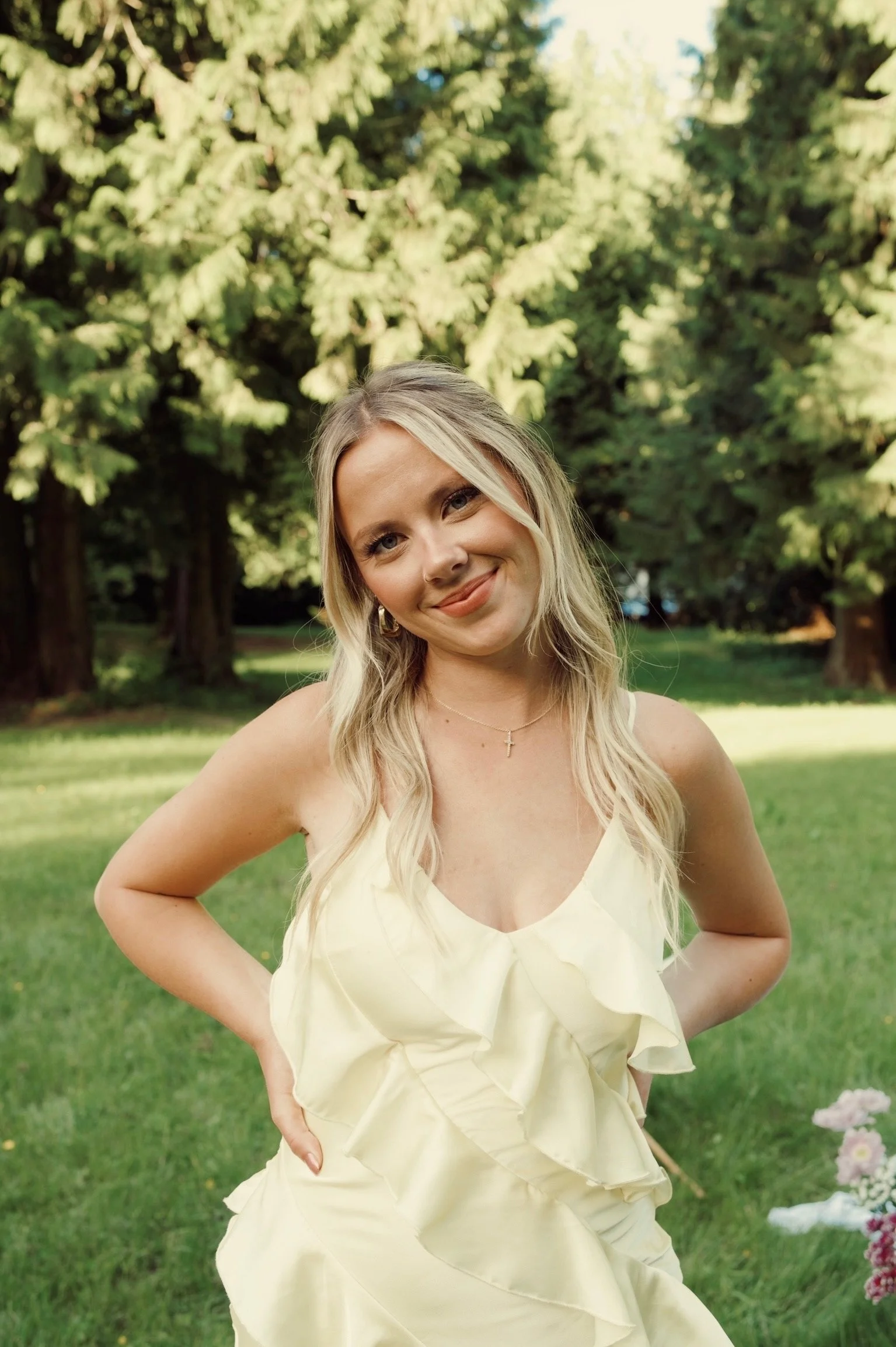 Hairstylist Caitlyn Deming standing in a sunlit garden wearing a pale yellow dress.