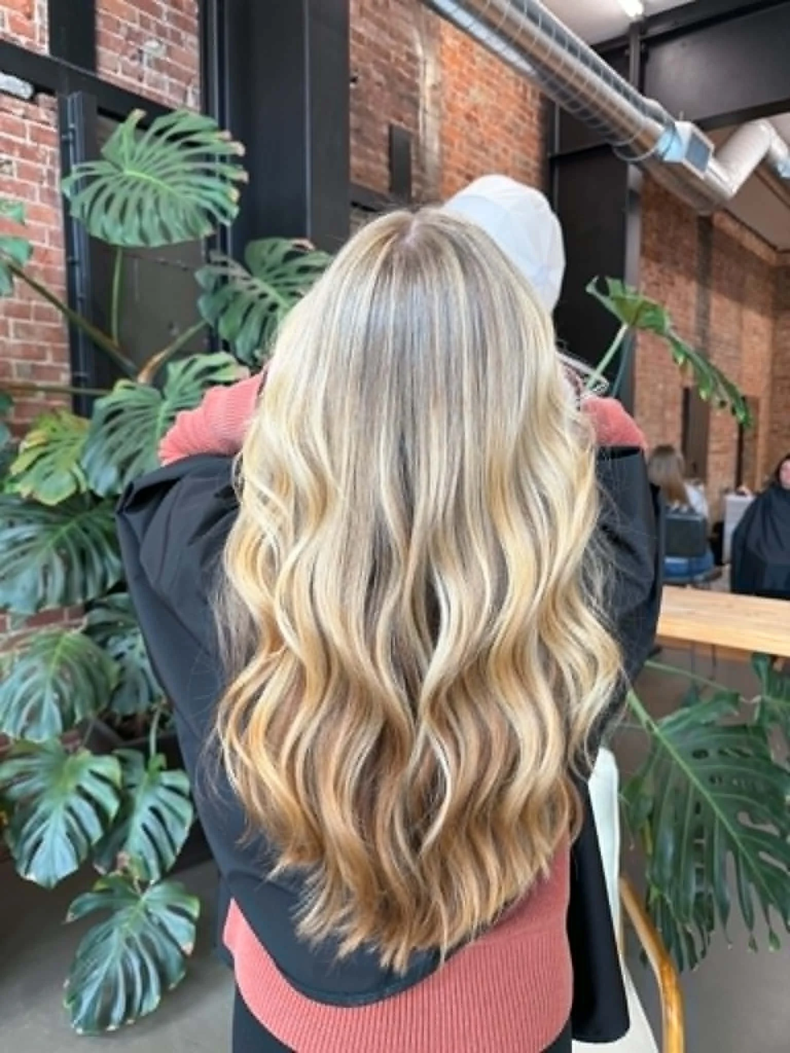 Back view of long blonde balayage with cascading waves and blended highlights by Caitlyn Deming.