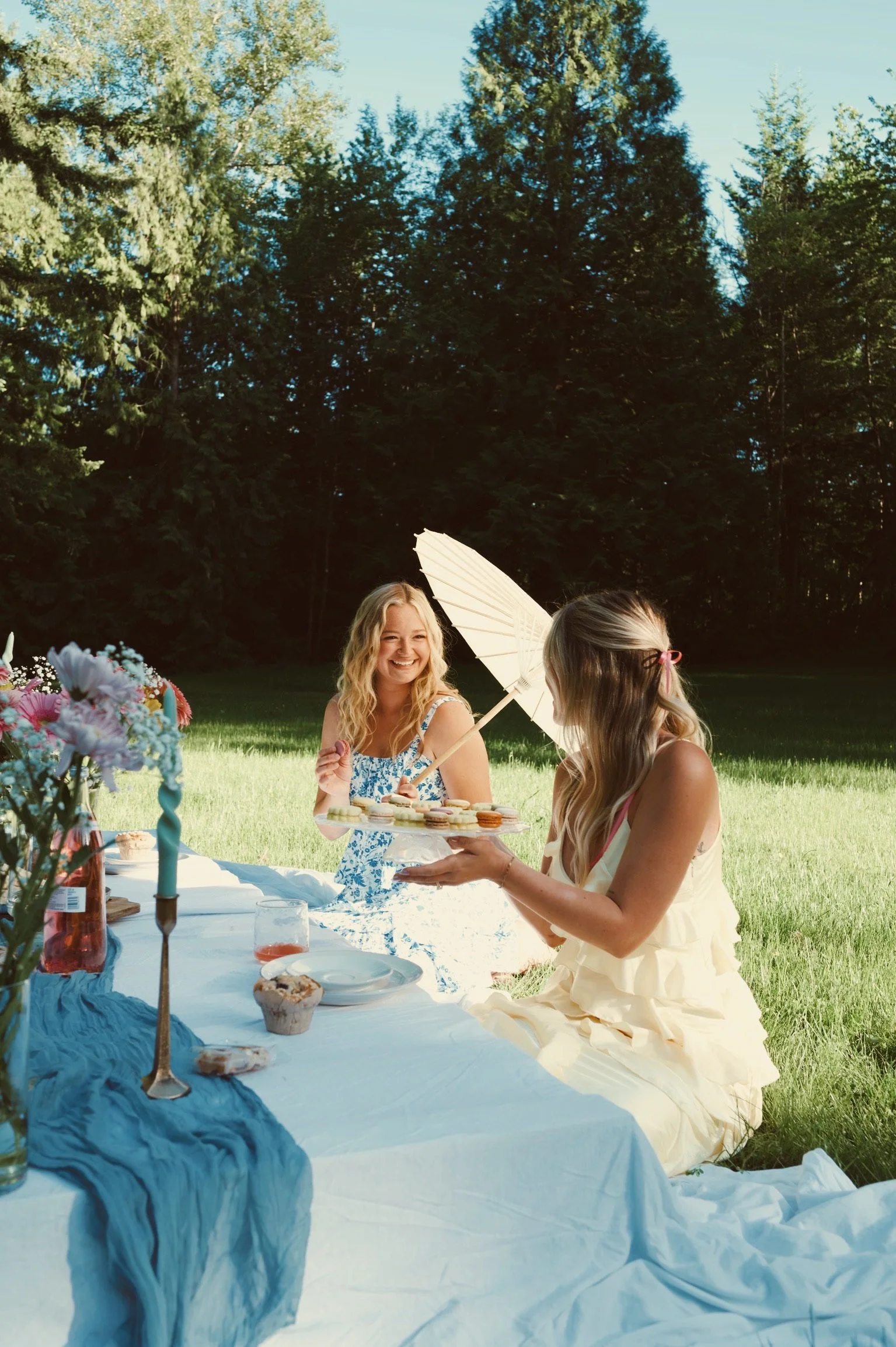 Friends gathered around a garden picnic table with flowers and refreshments during Caitlyn Deming’s branding photoshoot.