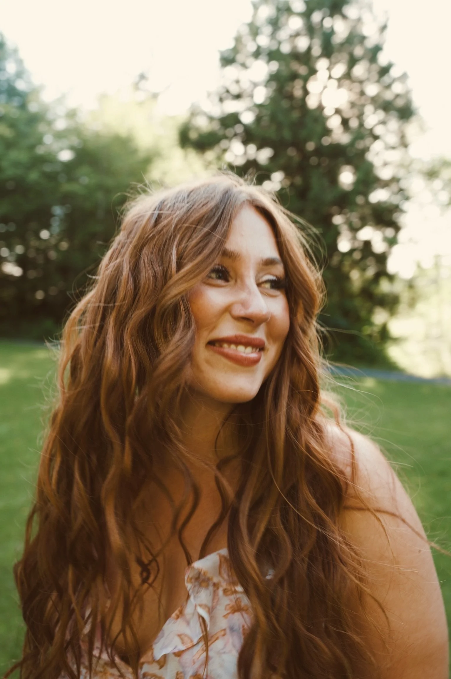 Woman with long, softly waved auburn hair in a garden portrait for Caitlyn Deming’s hairstyling portfolio.