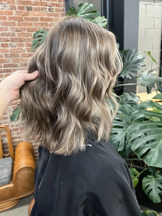 Woman with shoulder-length bronde waves and dimensional color by Caitlyn Deming.