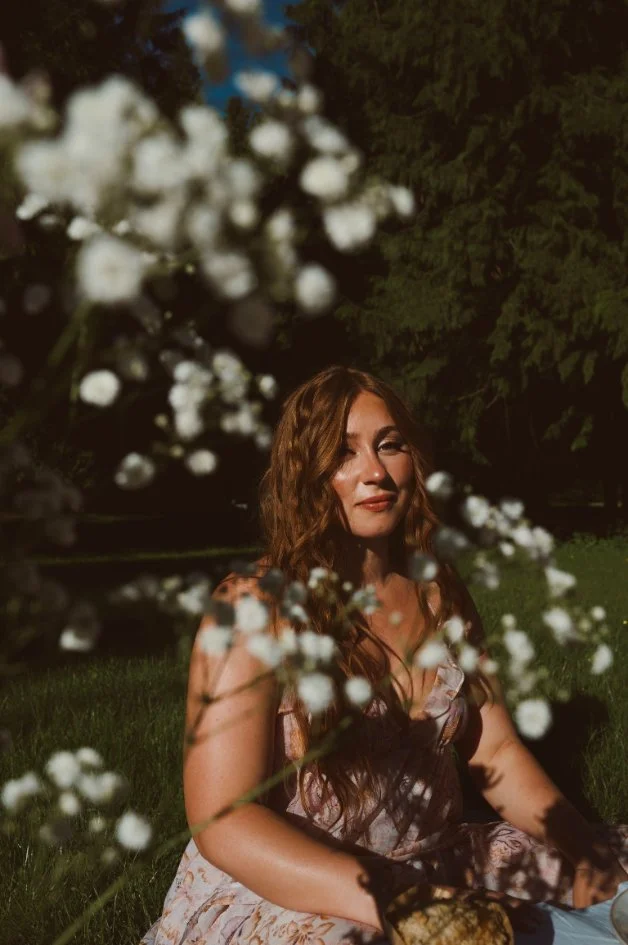Woman with long brown hair photographed in soft, moody garden light.