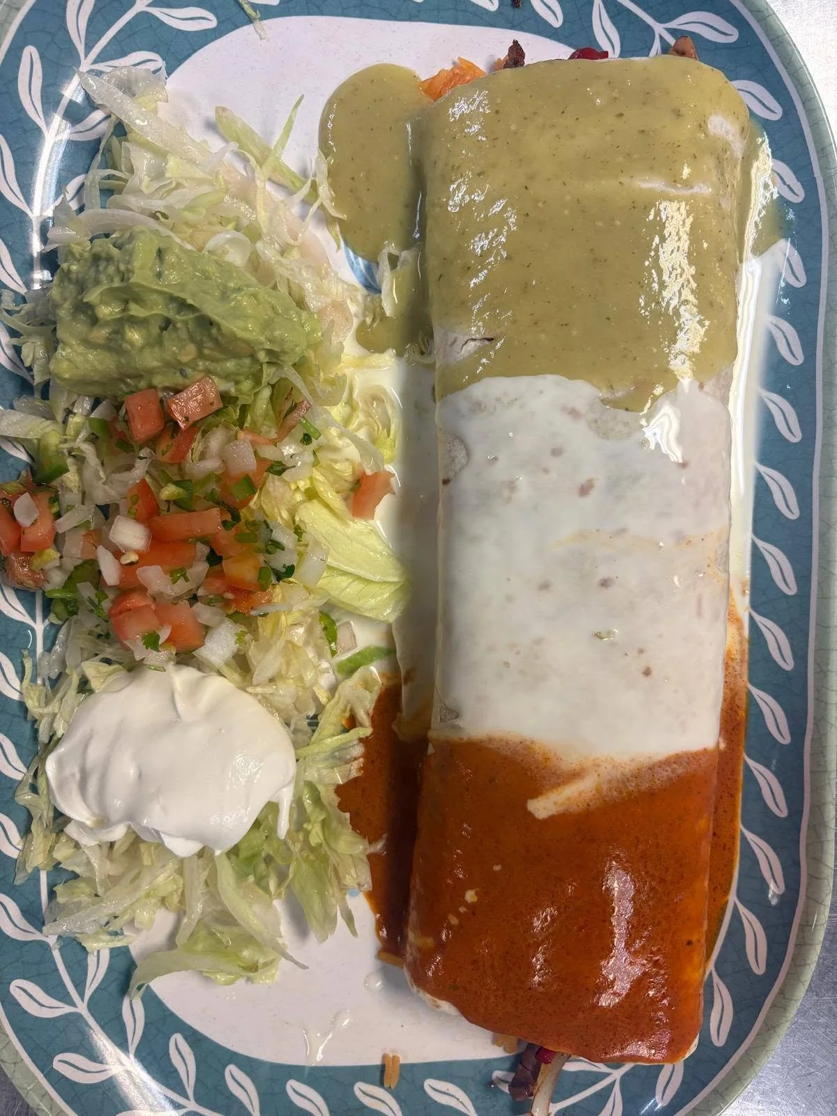 Plate with two enchiladas topped with different sauces, Mexican rice, and a side salad with lettuce, tomato, onion, guacamole, sour cream, and mayonnaise.