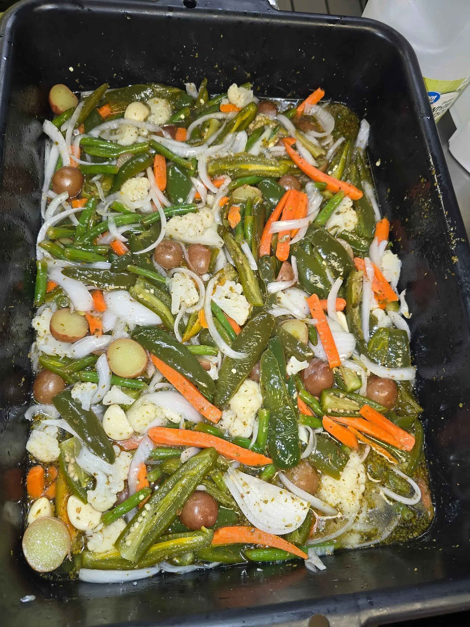 A pan filled with cooked mixed vegetables including green beans, cauliflower, carrots, onions, potatoes, and various seasonings.