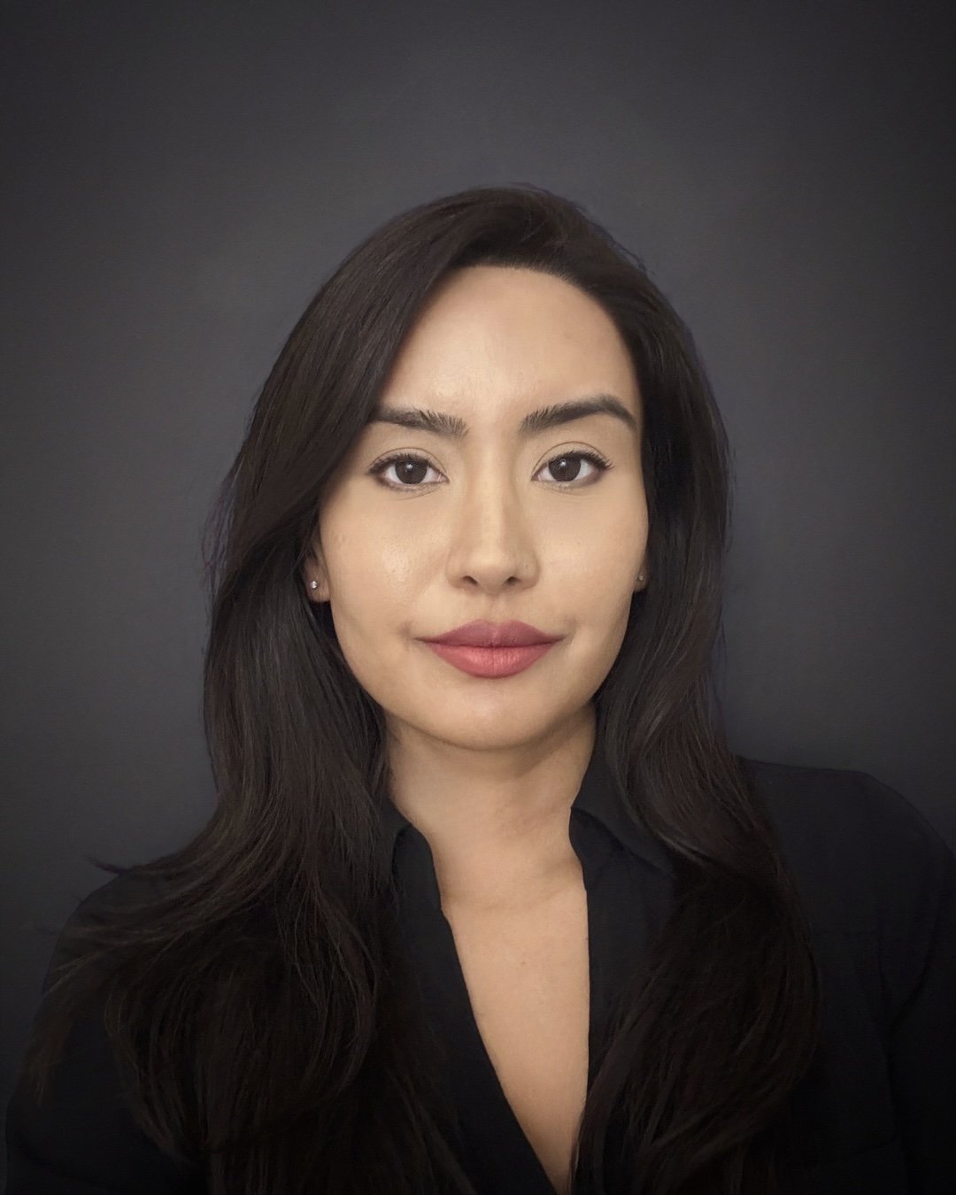 Portrait of a woman with long dark hair, wearing a black top, against a dark background.