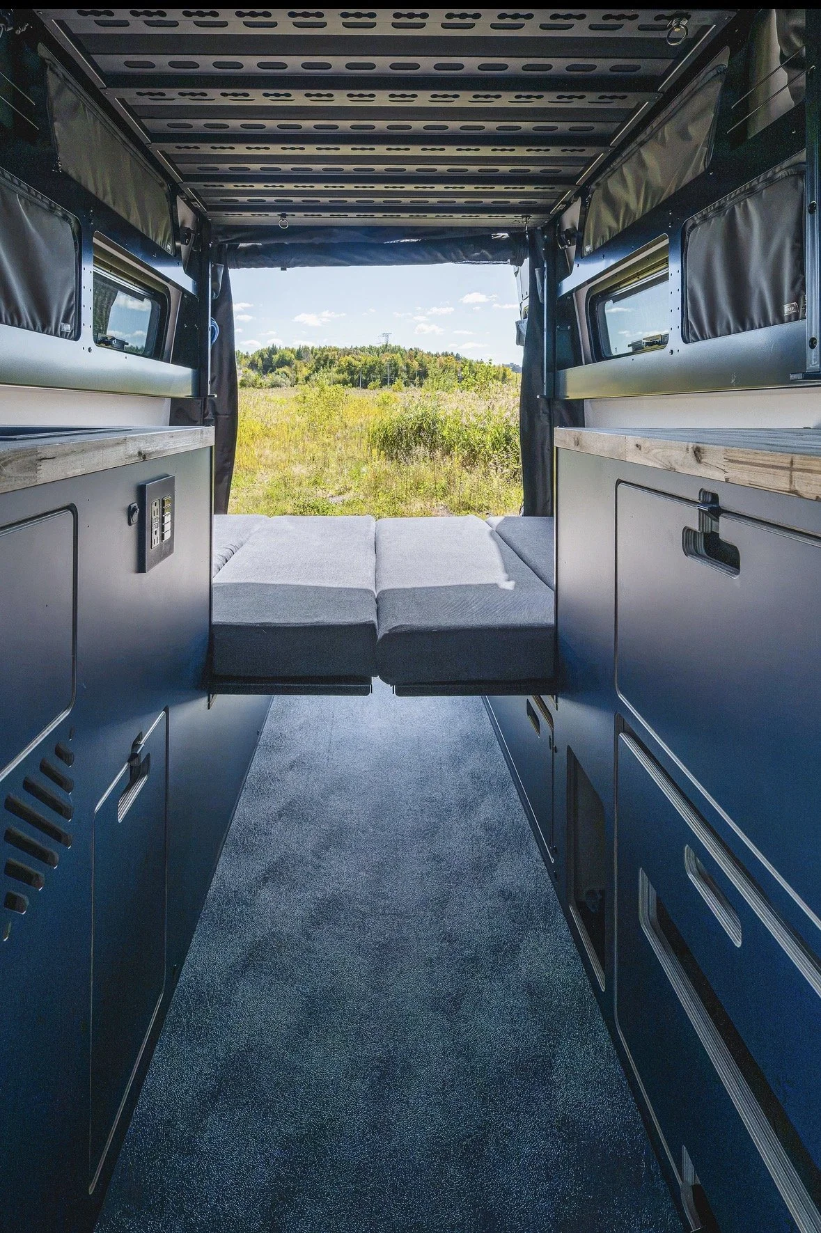 Espace de couchage du Hervé G2 avec lit à l'arrière, mobilier intégré et vue sur la nature par les portes arrière.