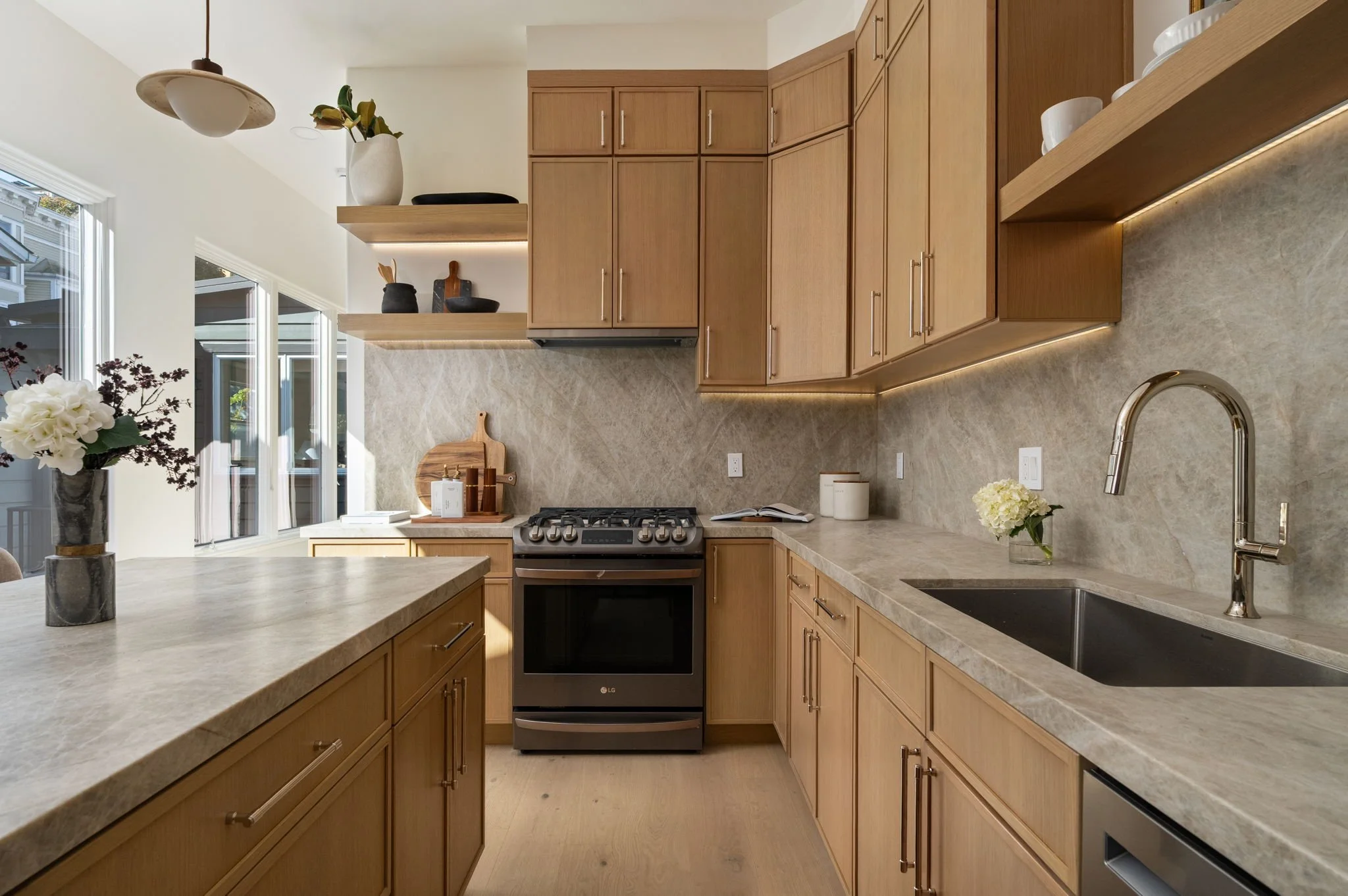 Modern kitchen with wooden cabinets, marble countertops, and a bouquet of white flowers on the counter.