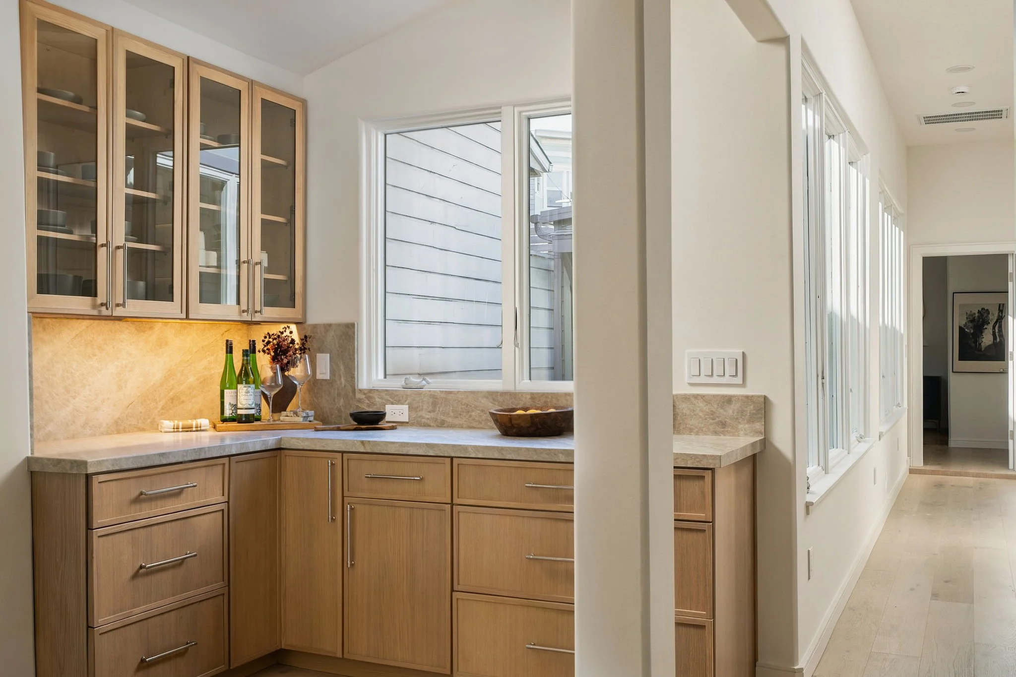 A kitchen with wooden cabinets, a beige marble countertop, and large windows allowing natural light in.