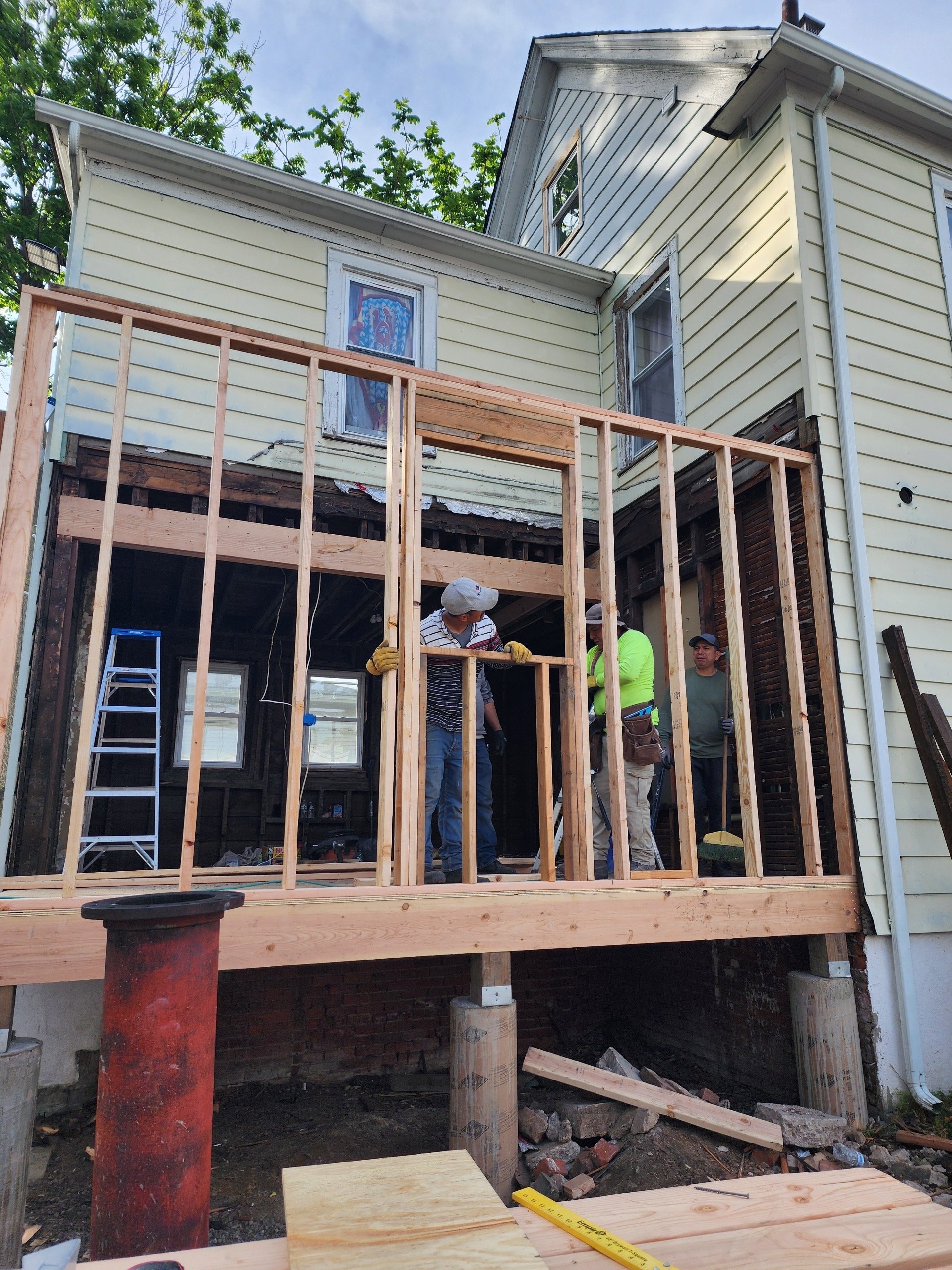 Construction workers building a deck at a residential house, with a partially framed structure and tools on site.