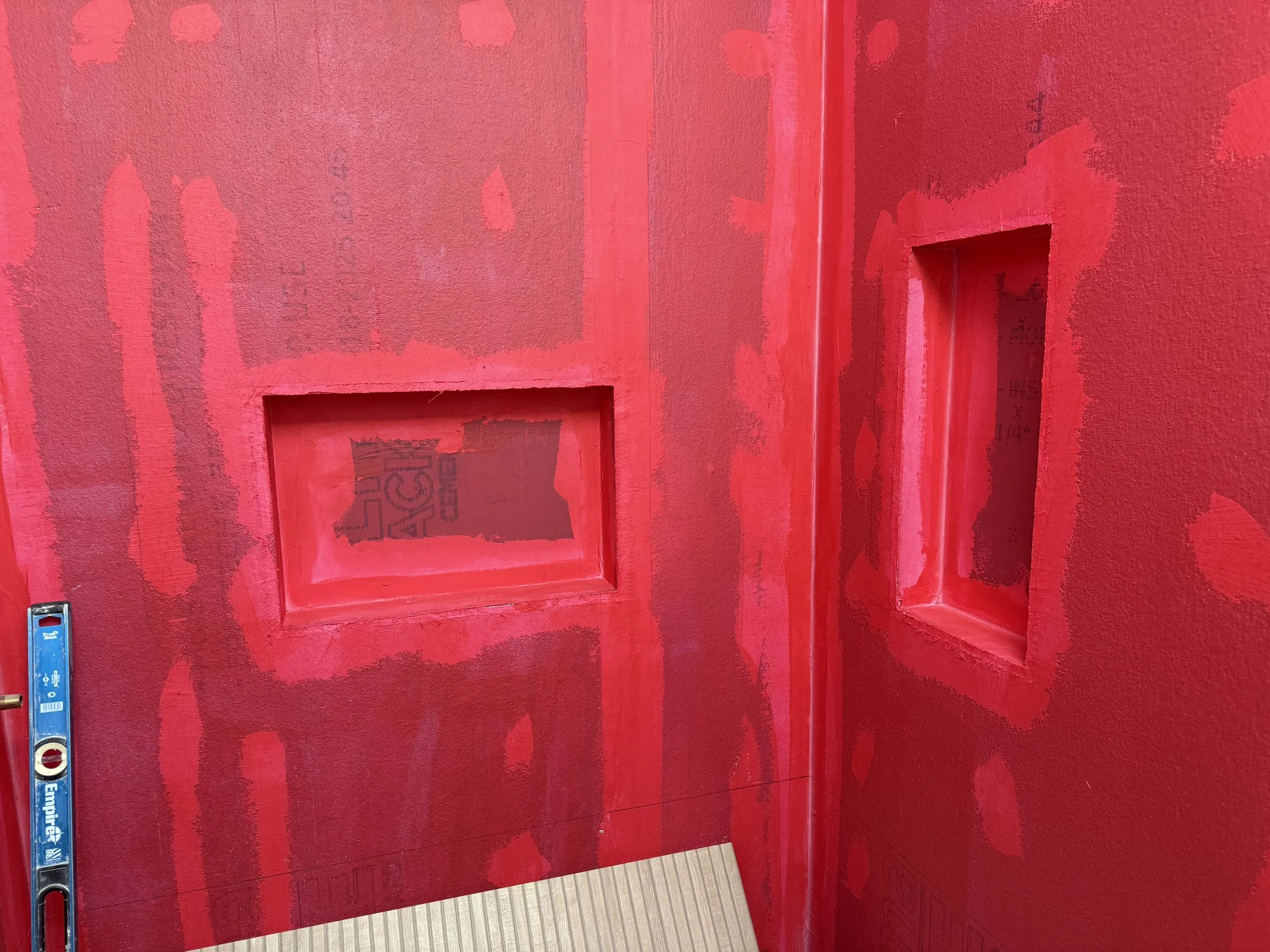 Red wall with unfinished patchwork paint, two rectangular cutouts, leveling tool on the floor.