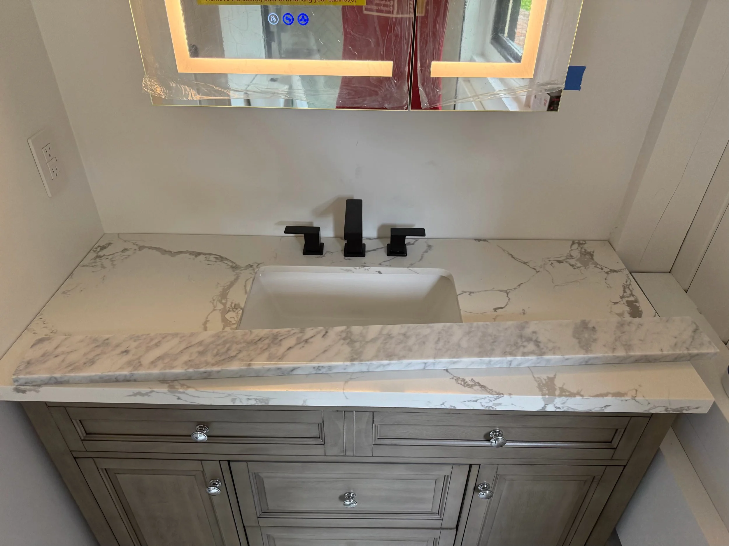 Bathroom vanity with a marble countertop, a sink, a faucet, and wooden cabinets with silver knobs.