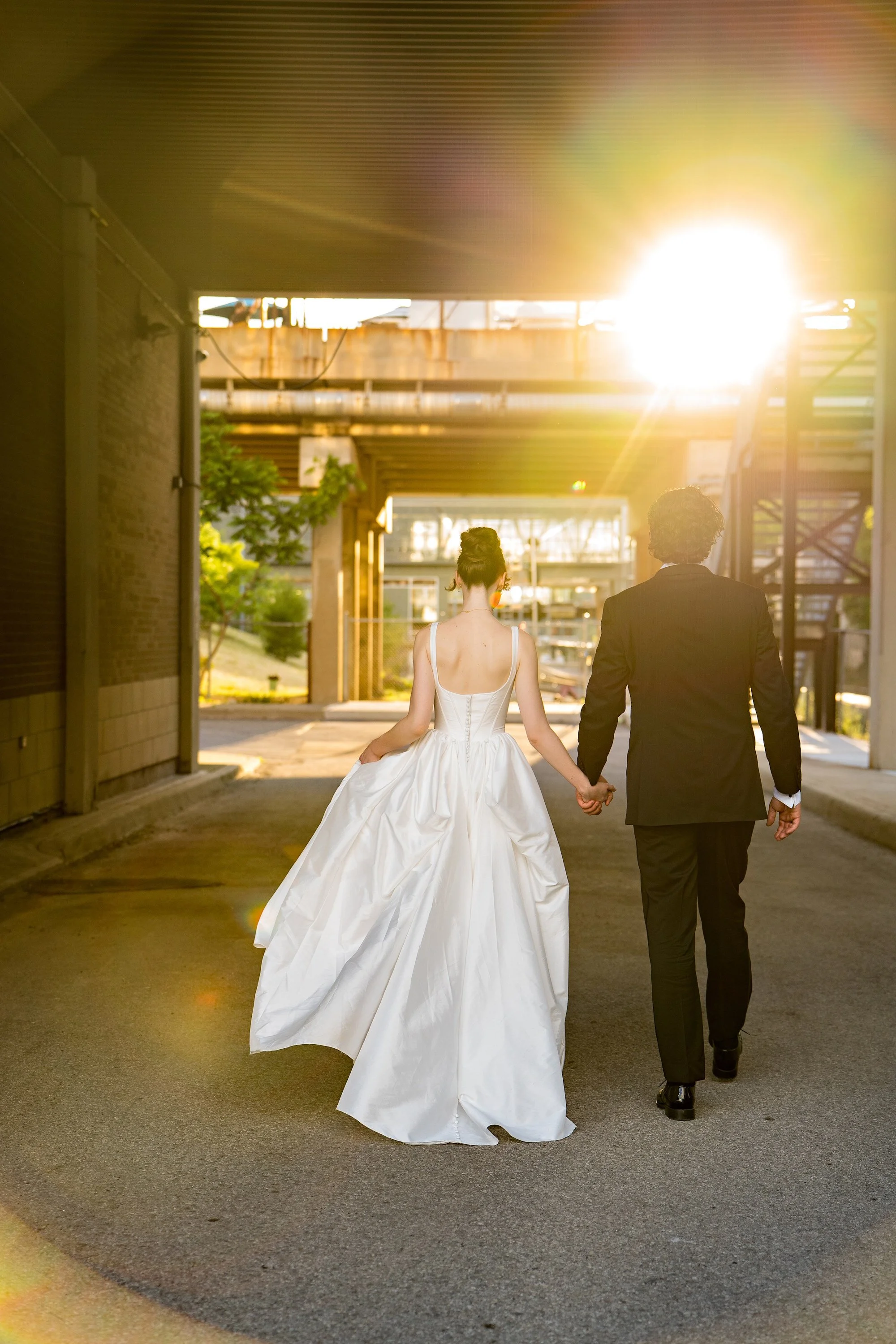 Bride walking towards the sunset with groom in hand. Beautiful and sleek high bun by Toronto makeup artist, Alanna