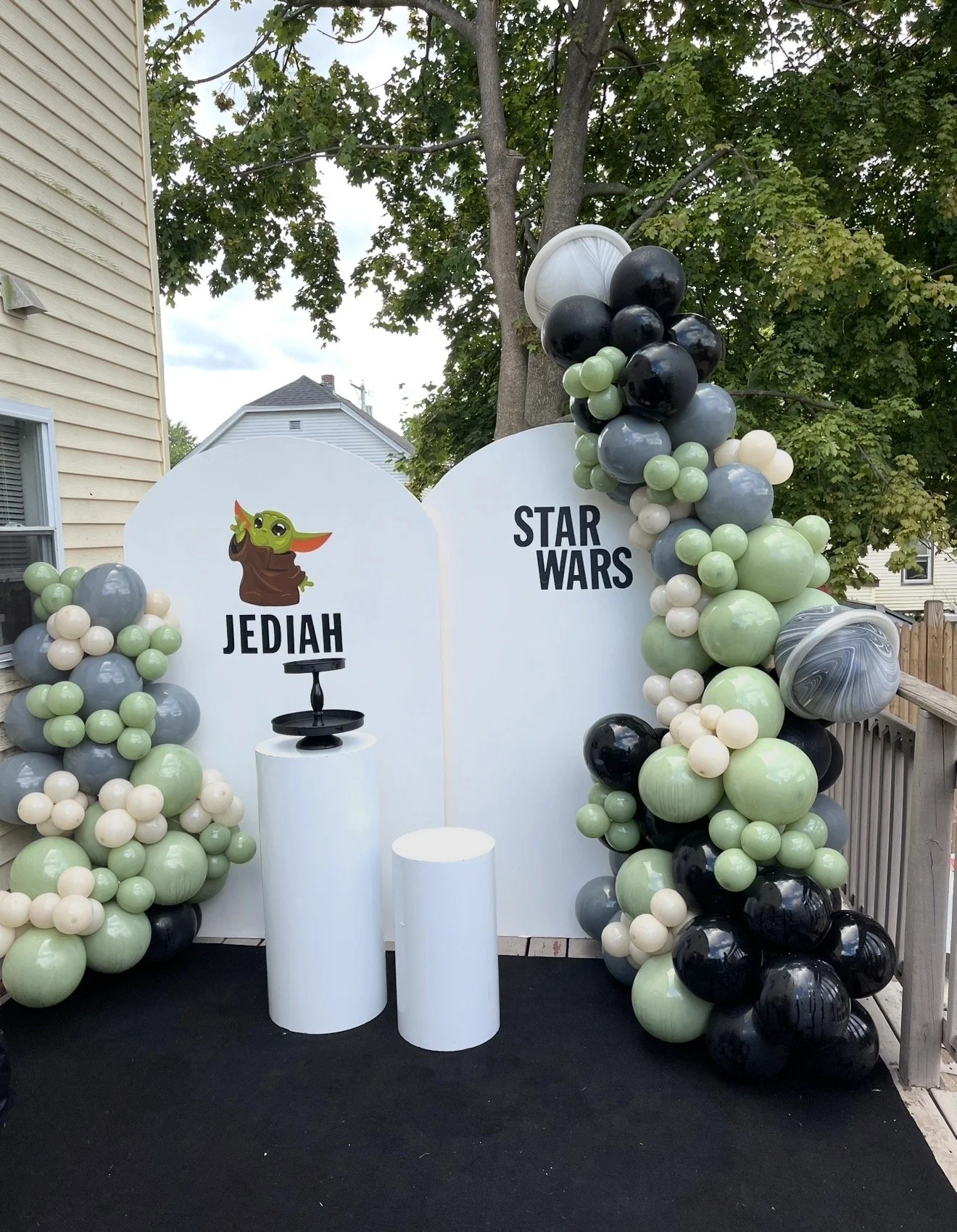 Star Wars-themed birthday party decoration with balloons in black, gray, white, and green, and a backdrop featuring "JEDIAH" with Baby Yoda illustration and a black cake stand.