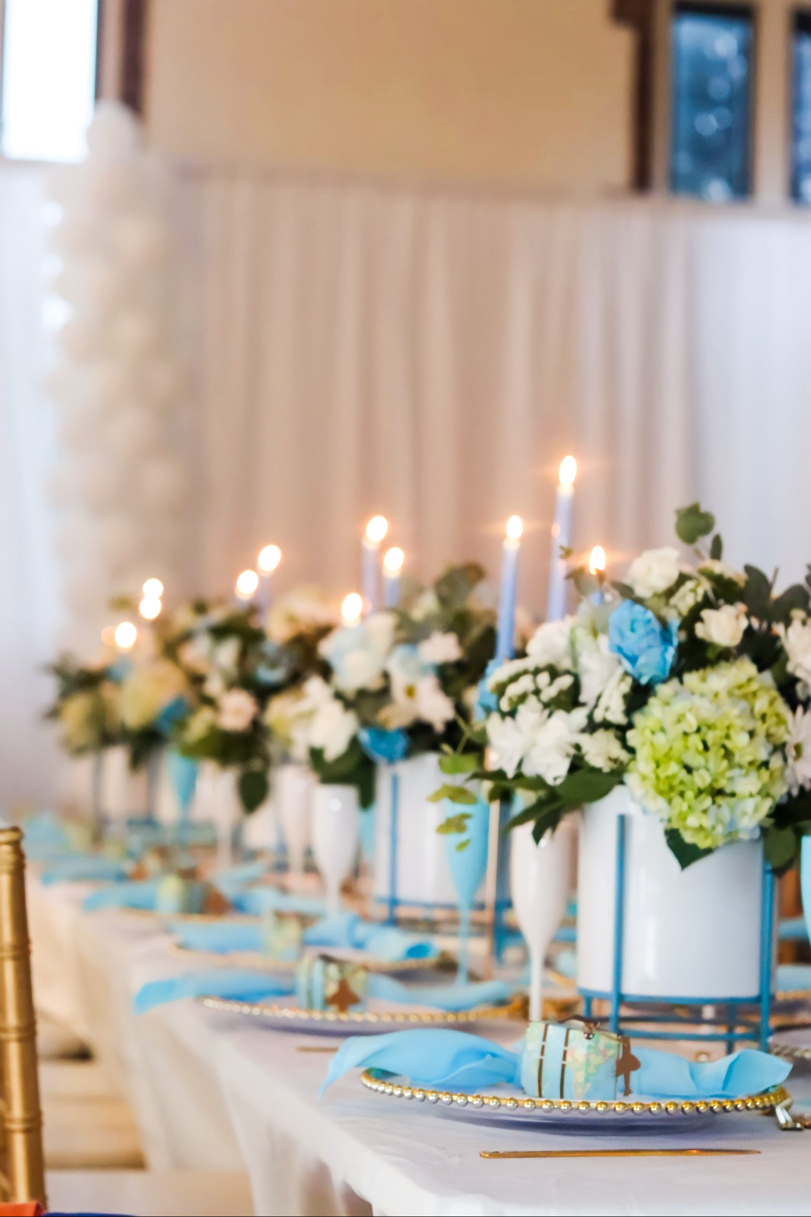 A decorated table with floral arrangements, blue and white candles, and elegant tableware at a celebration or wedding reception.