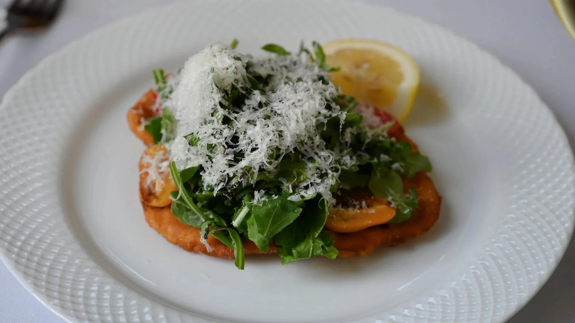 A plate with toast topped with arugula, shredded cheese, and lemon wedge on the side.