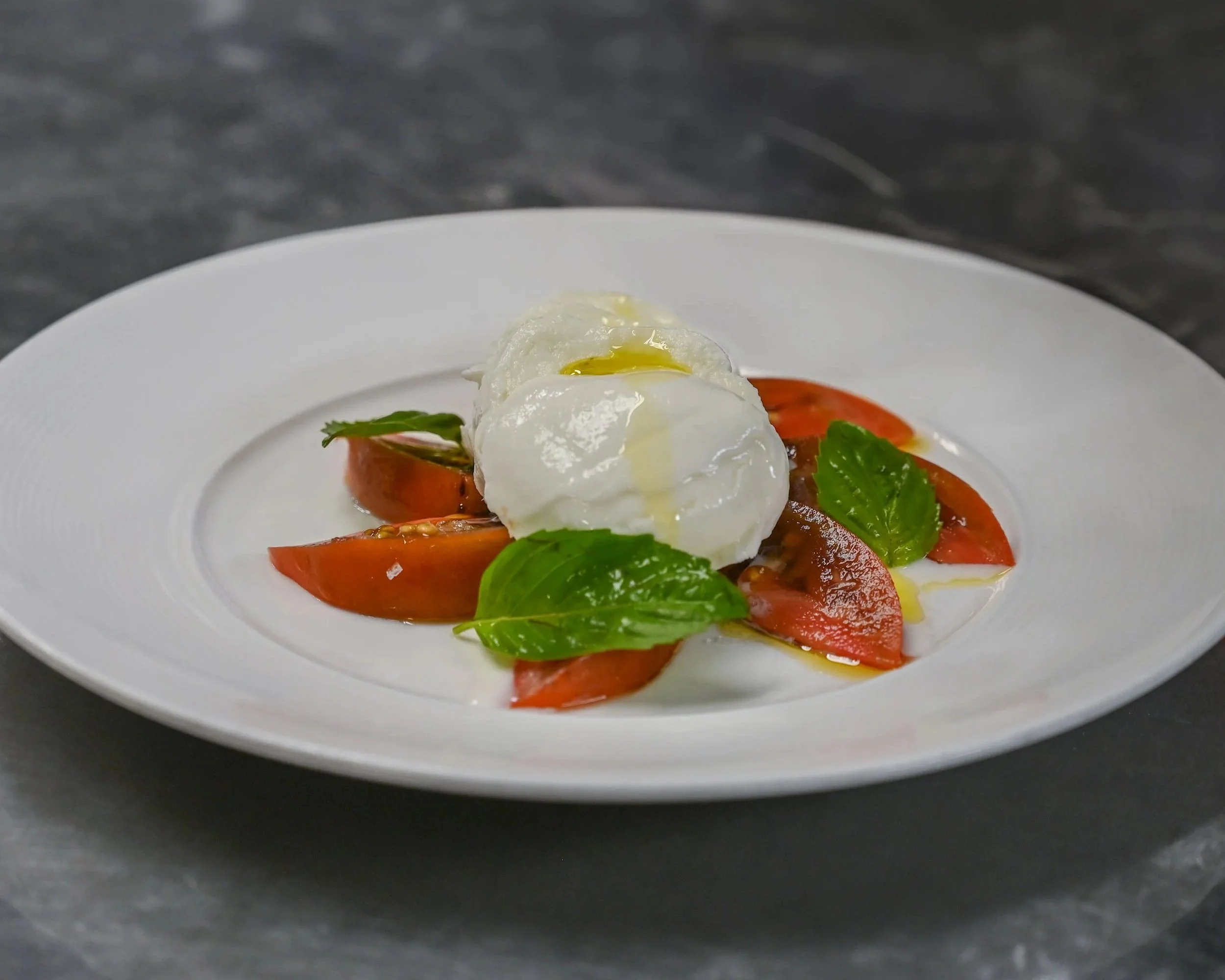 Poached eggs on a bed of sliced tomatoes and fresh basil leaves served on a white plate.